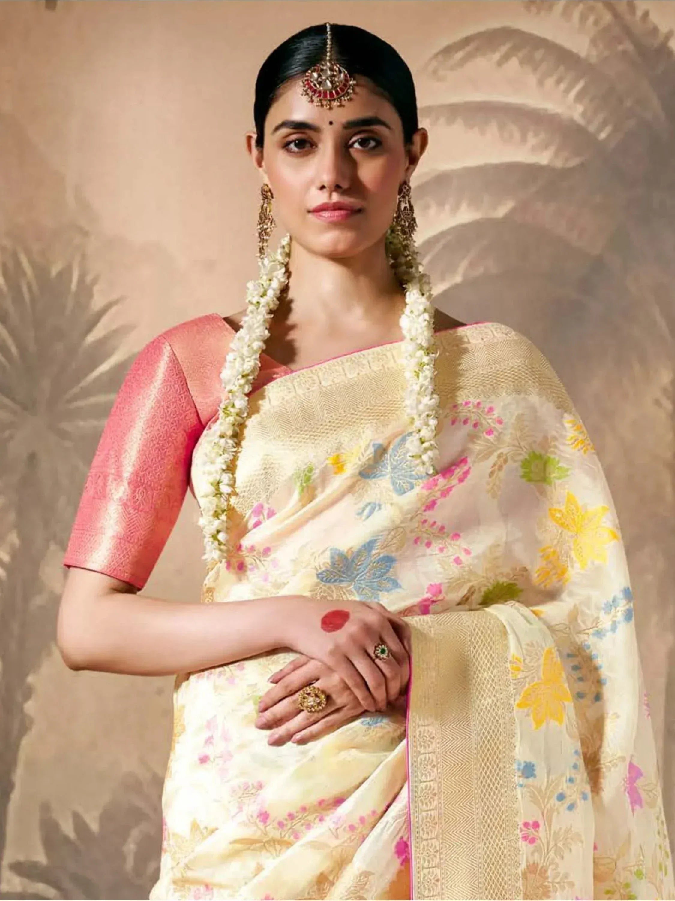 Woman in floral printed saree with pink blouse, traditional jewelry, and flower garland