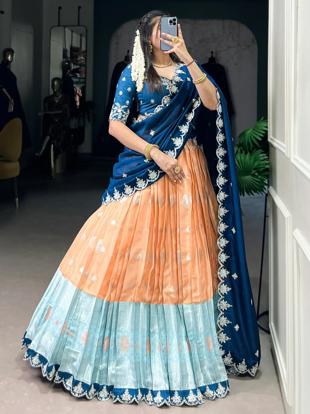 Woman in blue and peach lehenga choli with white embroidery, taking mirror selfie in boutique