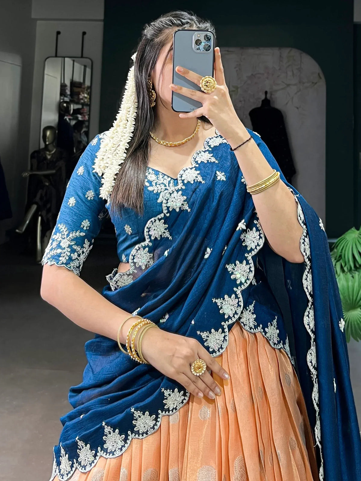 Blue embroidered saree with peach lehenga, gold jewelry, and floral hair accessory for Indian ethnic wear