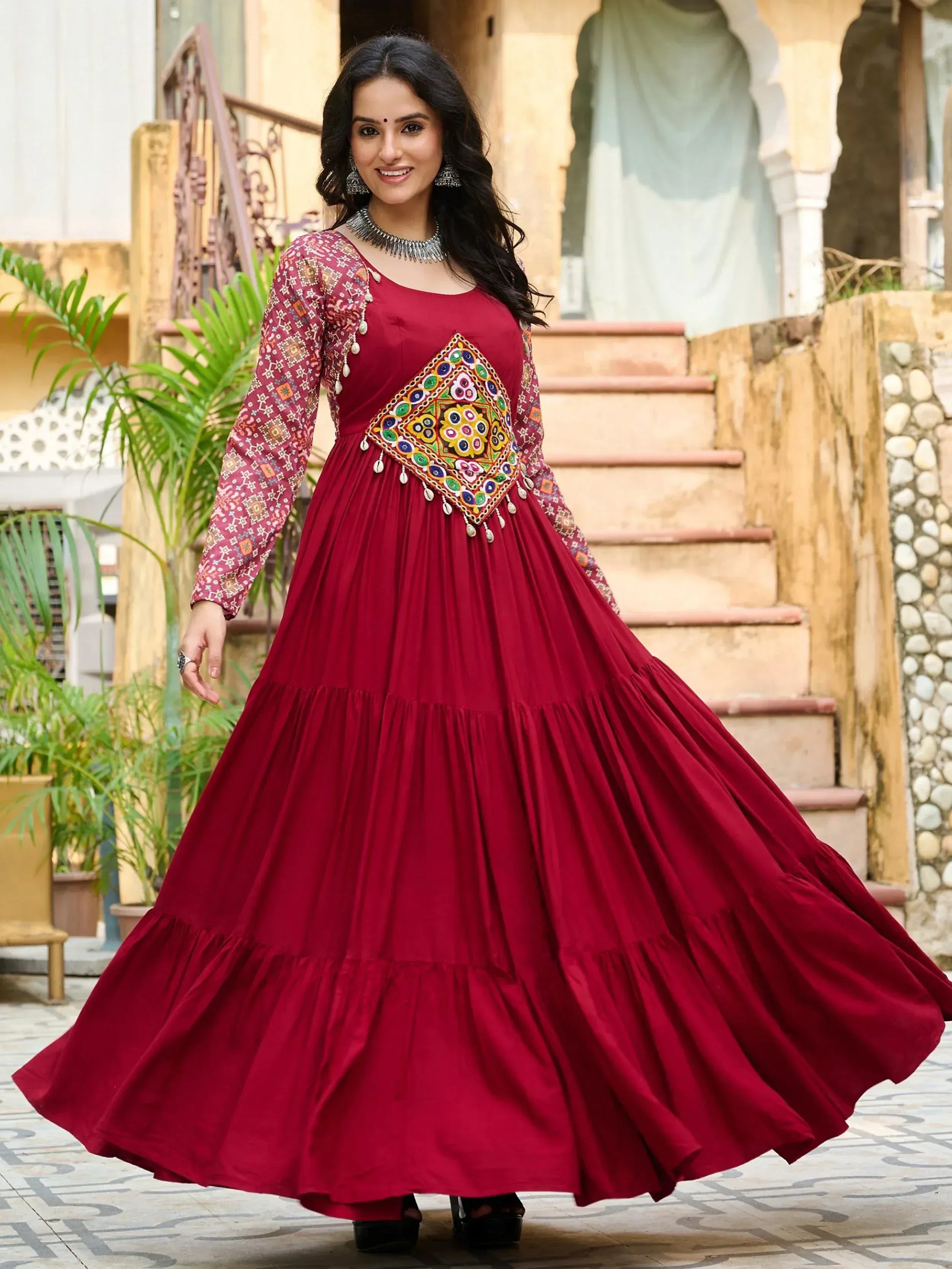 Maroon ethnic gown with mirror work and tiered skirt, perfect for Indian occasions