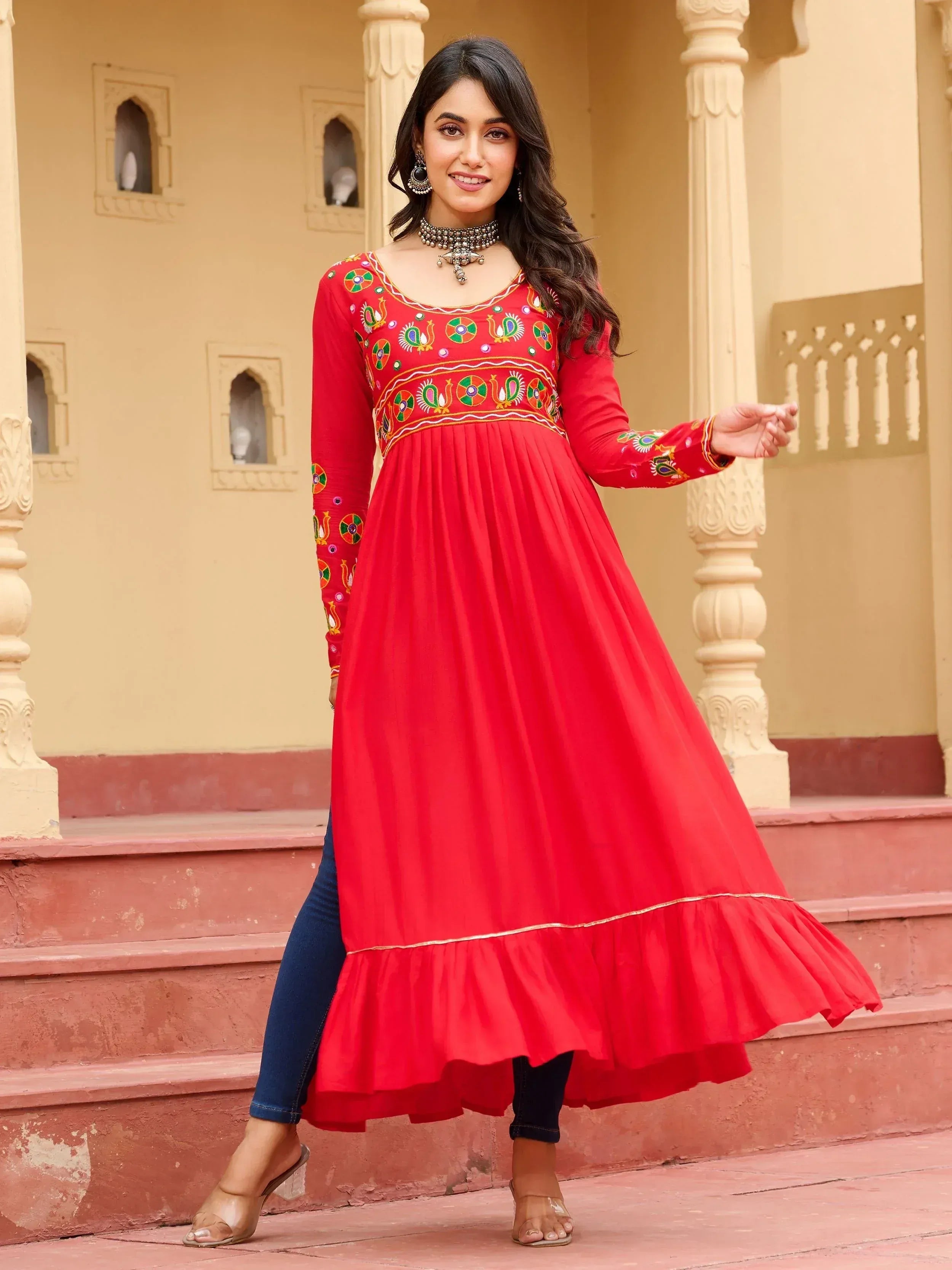 Red embroidered ethnic gown with peacock motifs, paired with jeans, perfect for Indian festive wear