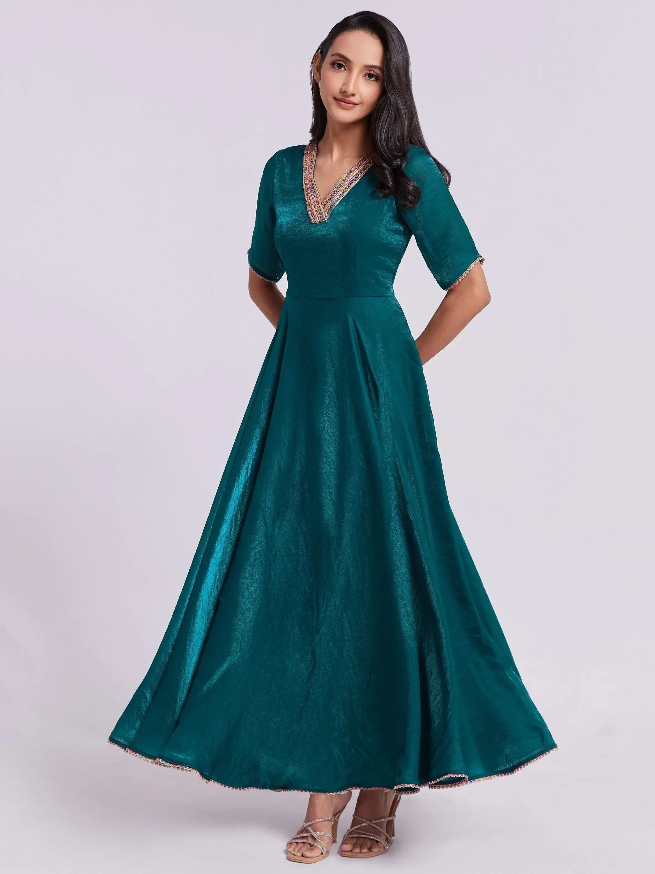 Woman wearing teal ethnic gown with half sleeves and embroidered V-neck, standing indoors