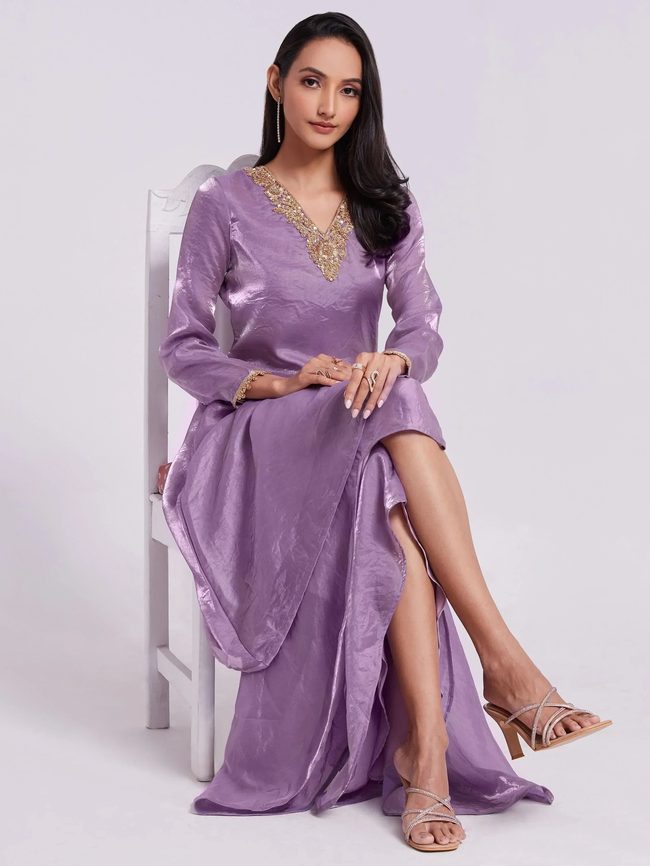 Woman in a lavender silk ethnic gown with gold embroidery, sitting on a white chair