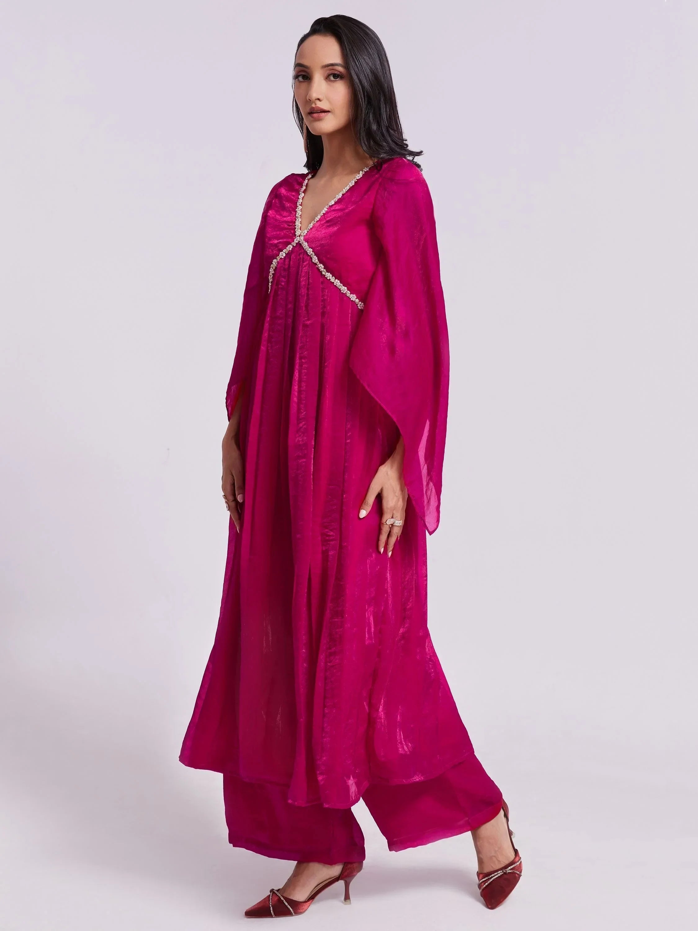 Woman in a bright pink ethnic gown with flared sleeves and embellishment, side pose