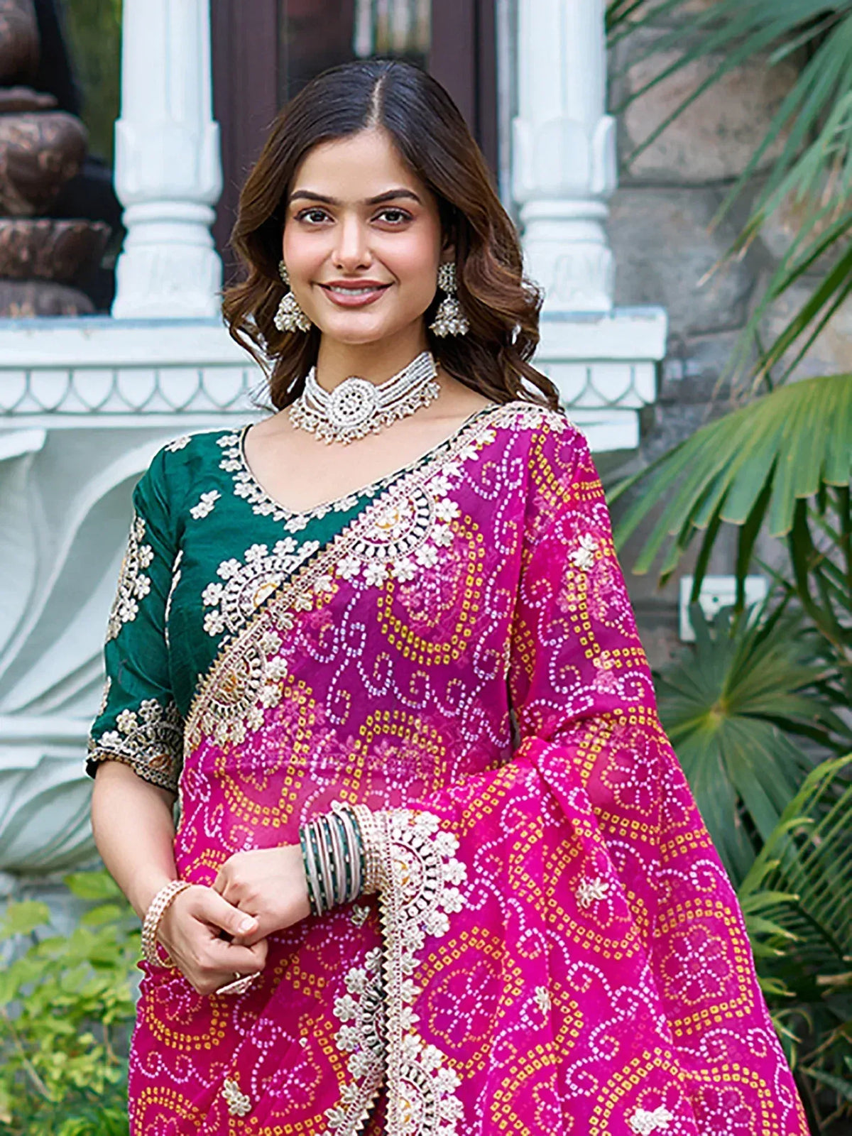 Woman in vibrant pink and green embroidered salwar kameez with traditional jewelry, perfect for Indian ethnic wear.