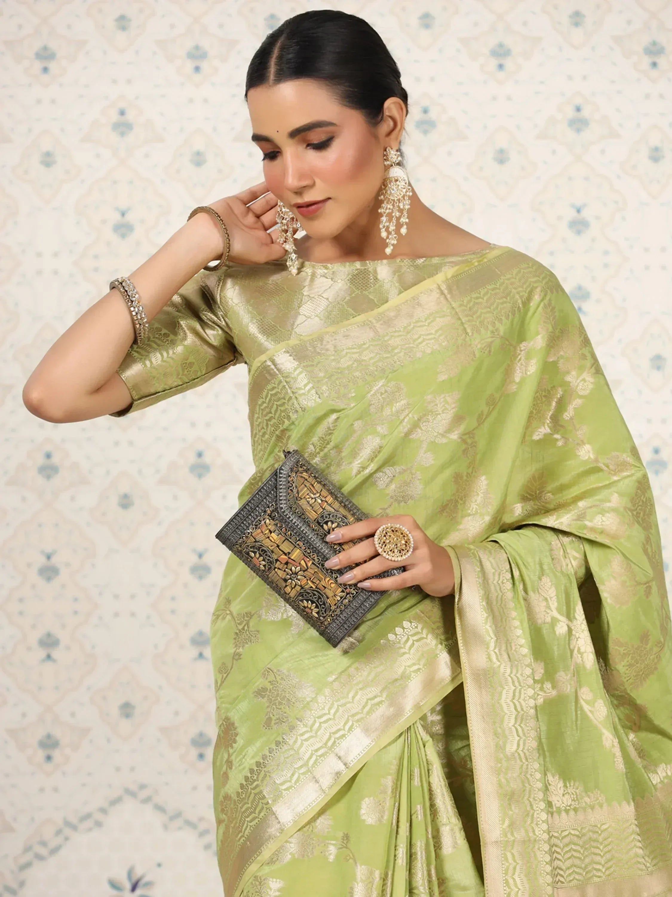 Elegant green saree with gold floral embroidery, paired with statement earrings and a decorative clutch.