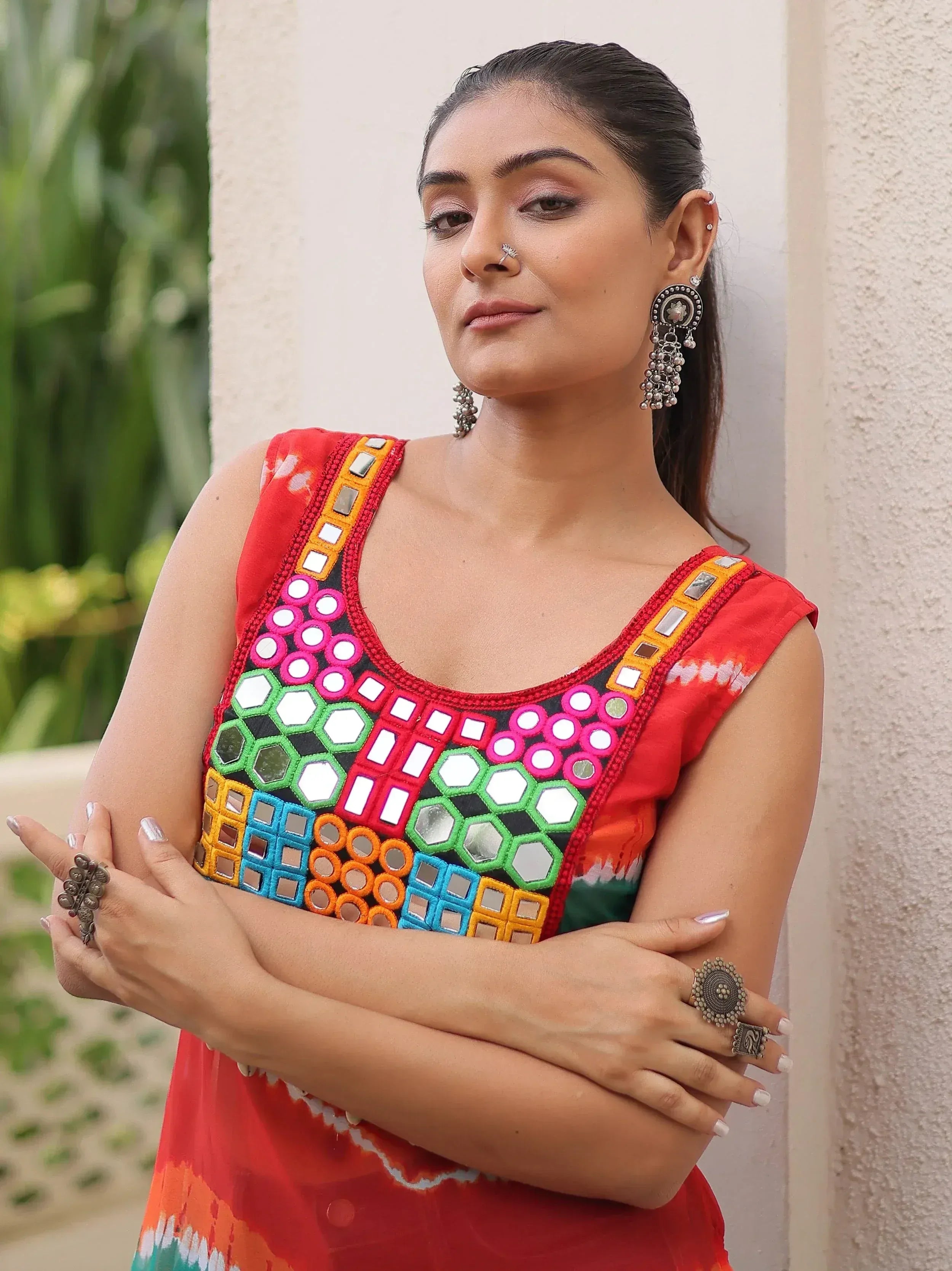 Woman in vibrant red ethnic top with mirror work and colorful embroidery, styled with traditional jewelry.