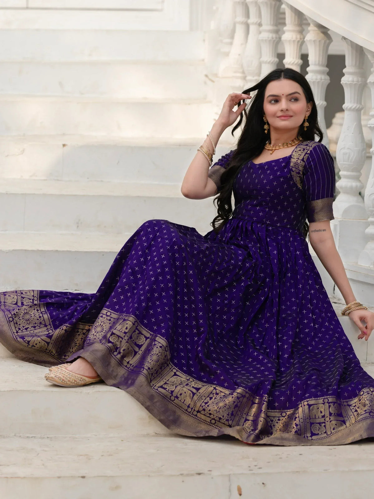 Woman in purple ethnic gown with gold elephant border, sitting on white marble steps