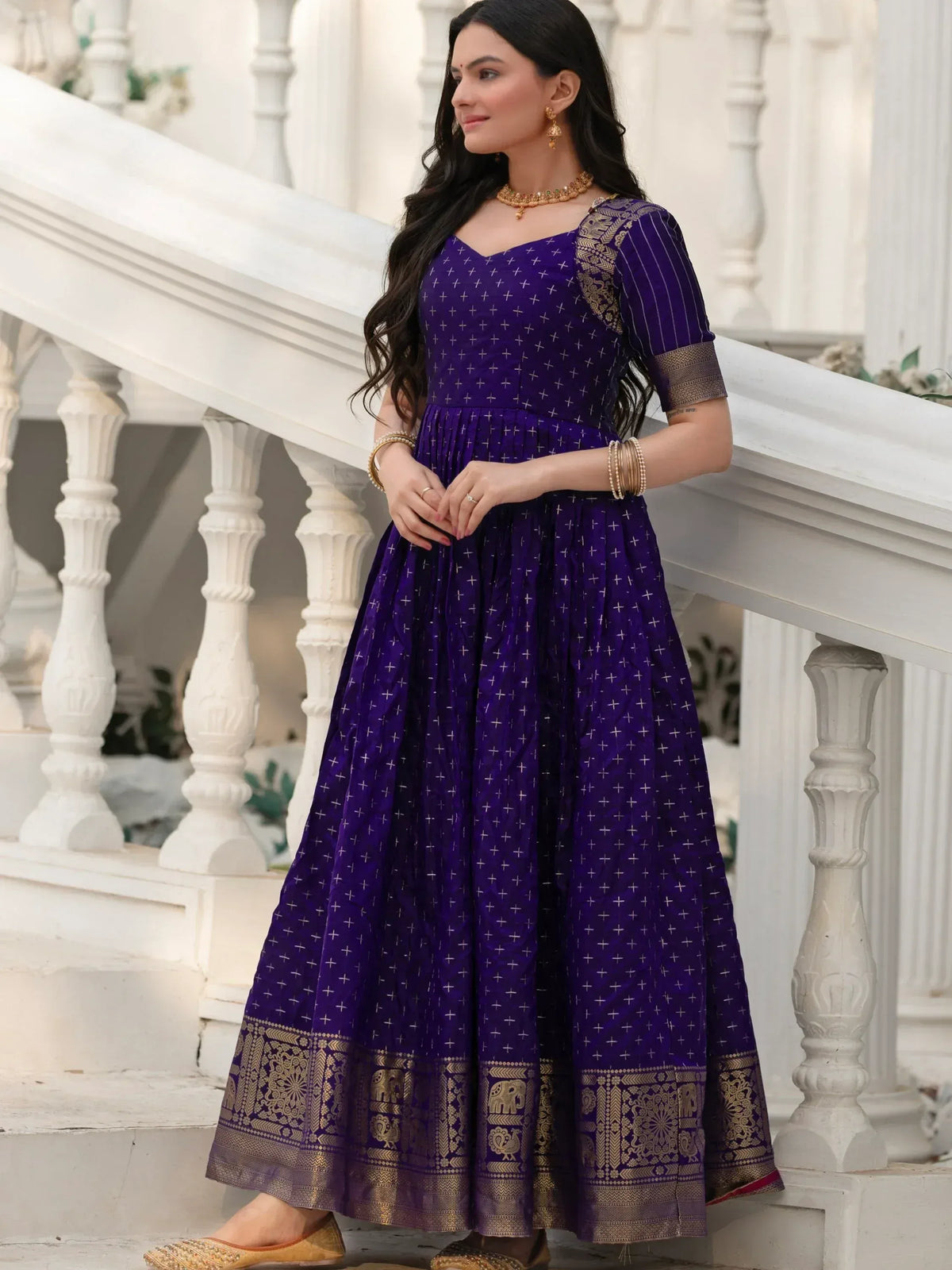 Purple ethnic gown with gold embroidery and elephant motifs, styled with traditional jewelry on white staircase