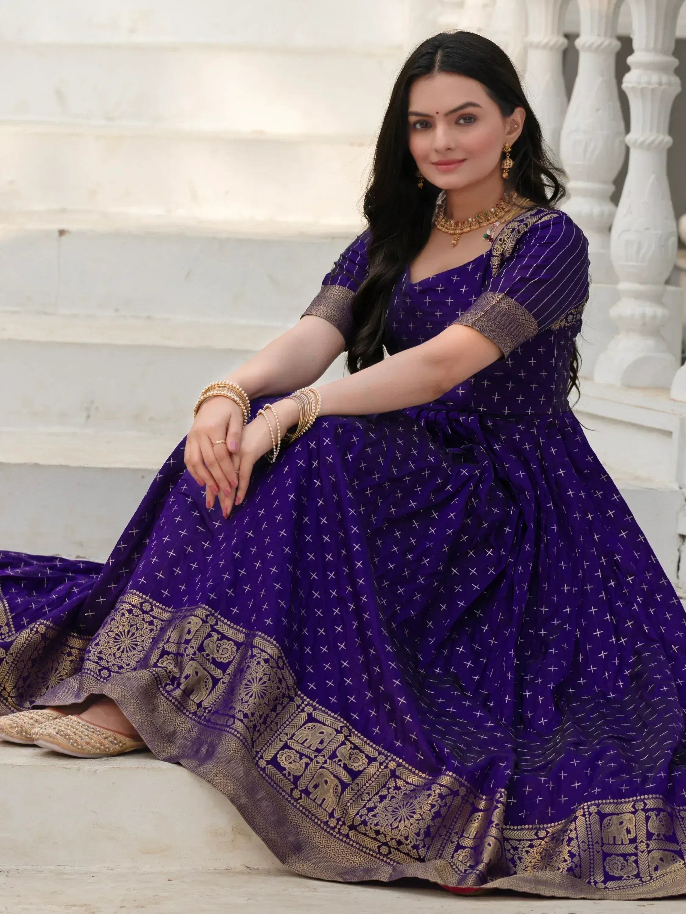 Woman in purple ethnic gown with gold elephant border, traditional Indian wear for festive occasions