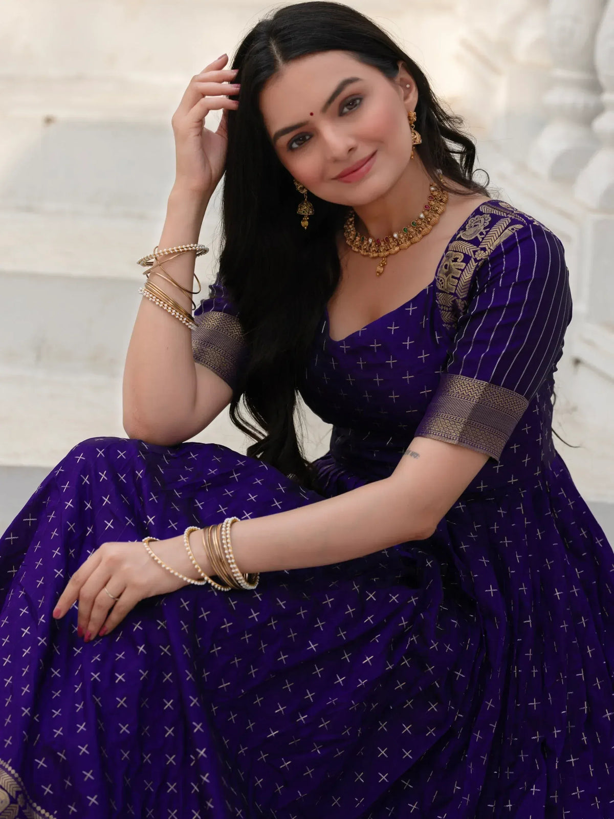 Woman in purple ethnic gown with gold embroidery, traditional jewelry, and cross pattern, perfect for Indian occasions.