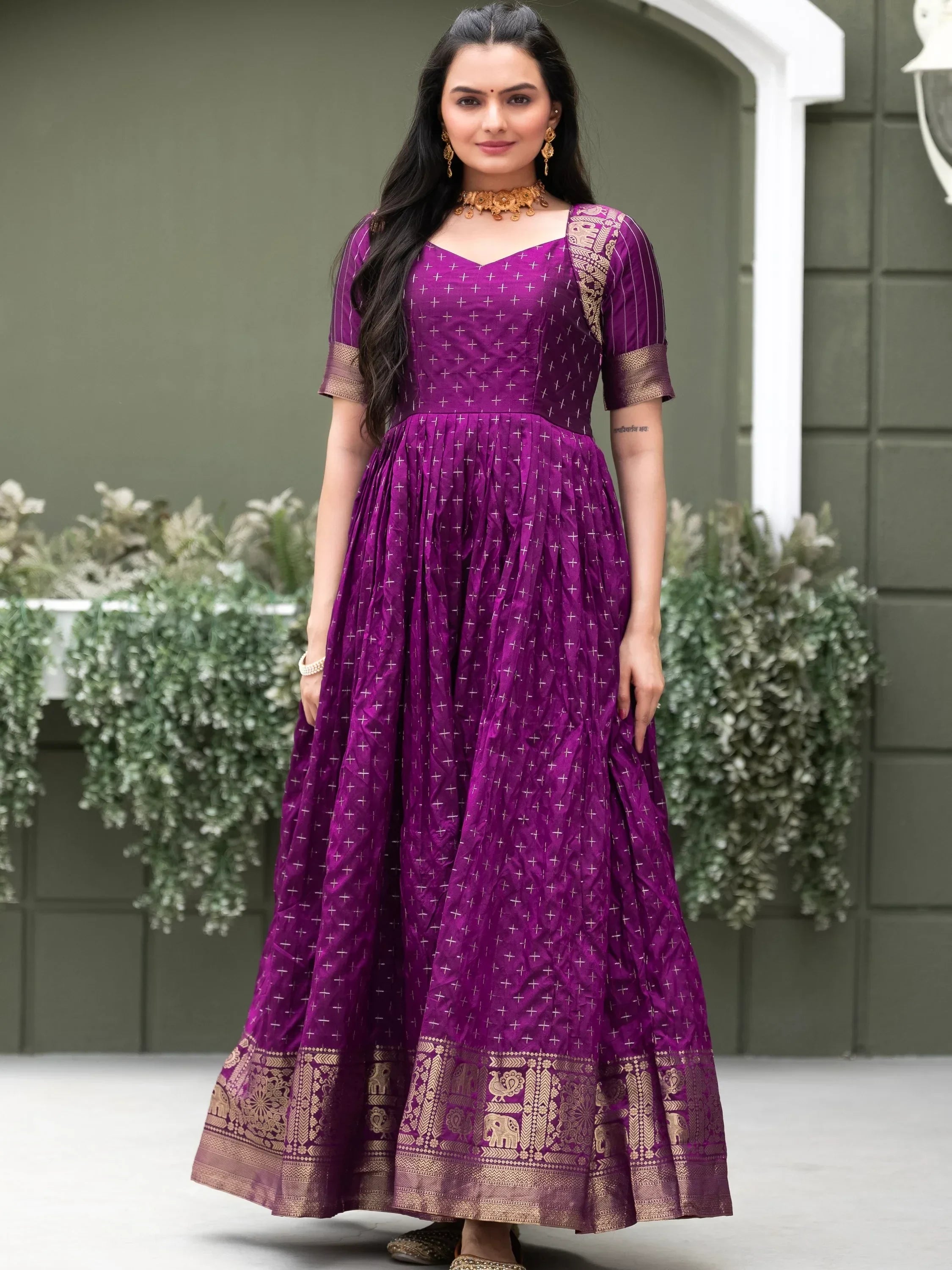 Woman in a purple Indian ethnic gown with gold embroidery and traditional jewelry