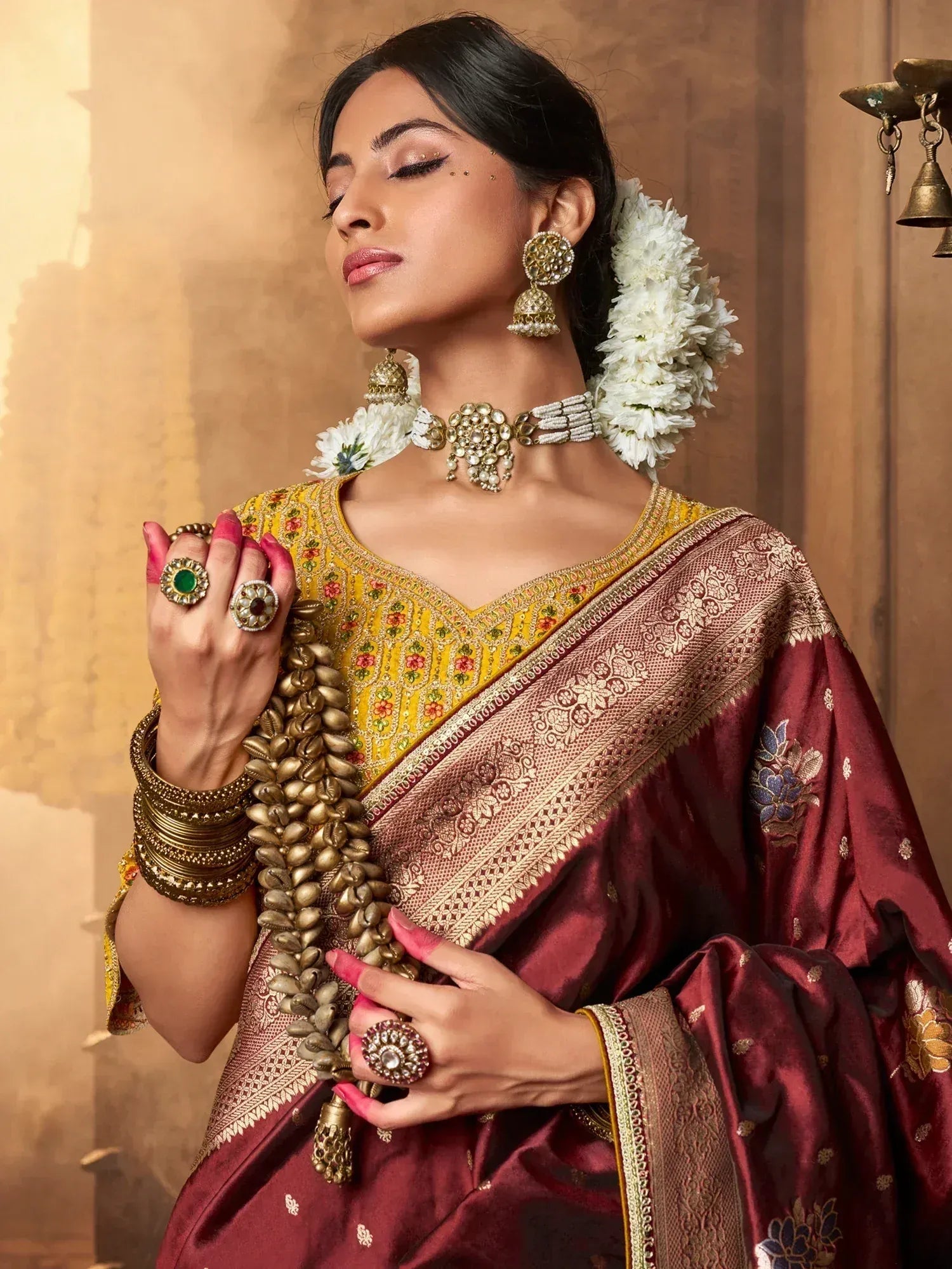 Elegant woman in maroon and gold embroidered saree with floral jewelry and white flowers in hair