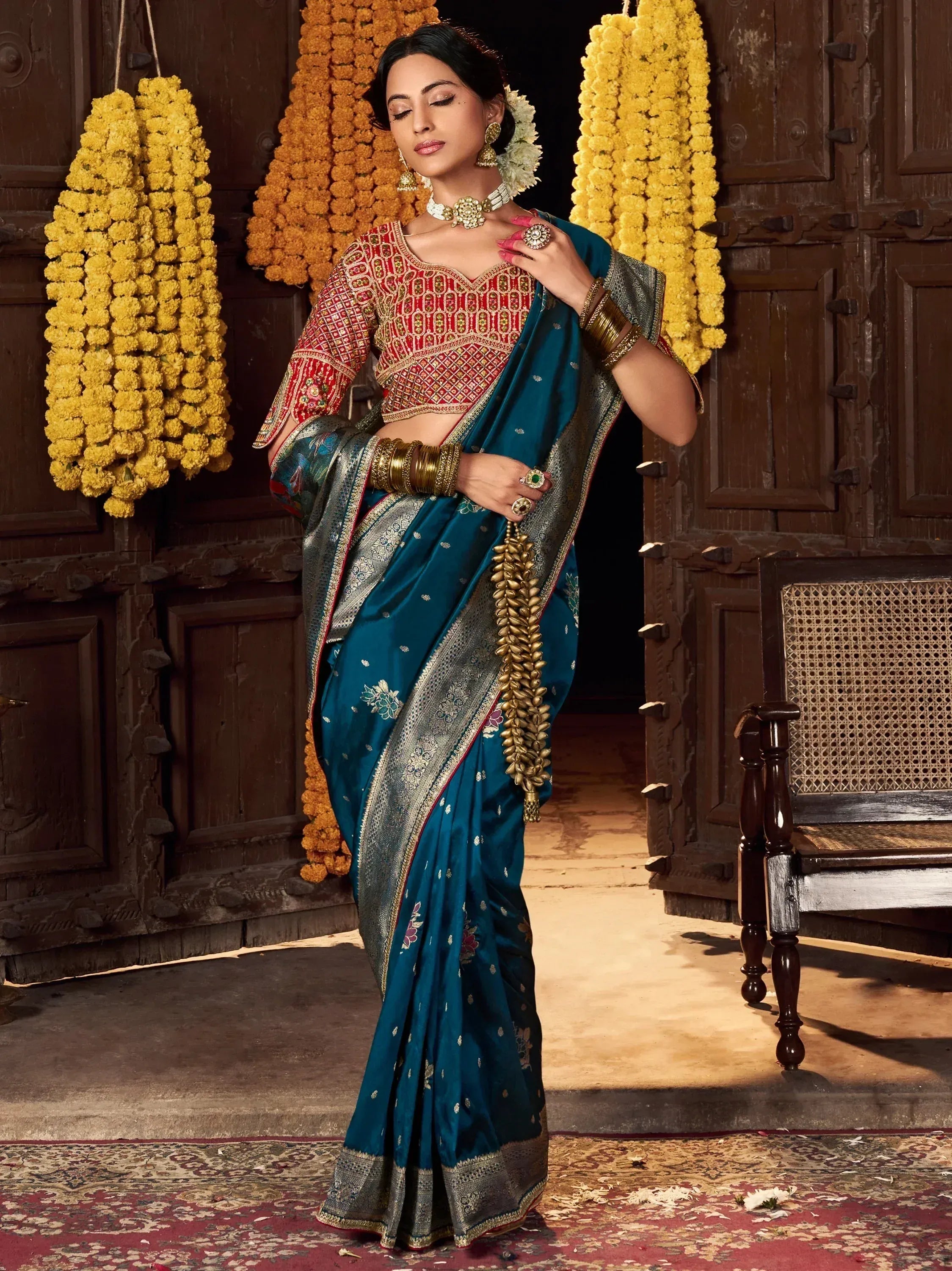 Teal silk saree with red embroidered blouse, gold jewelry, and floral garlands for Indian ethnic wear