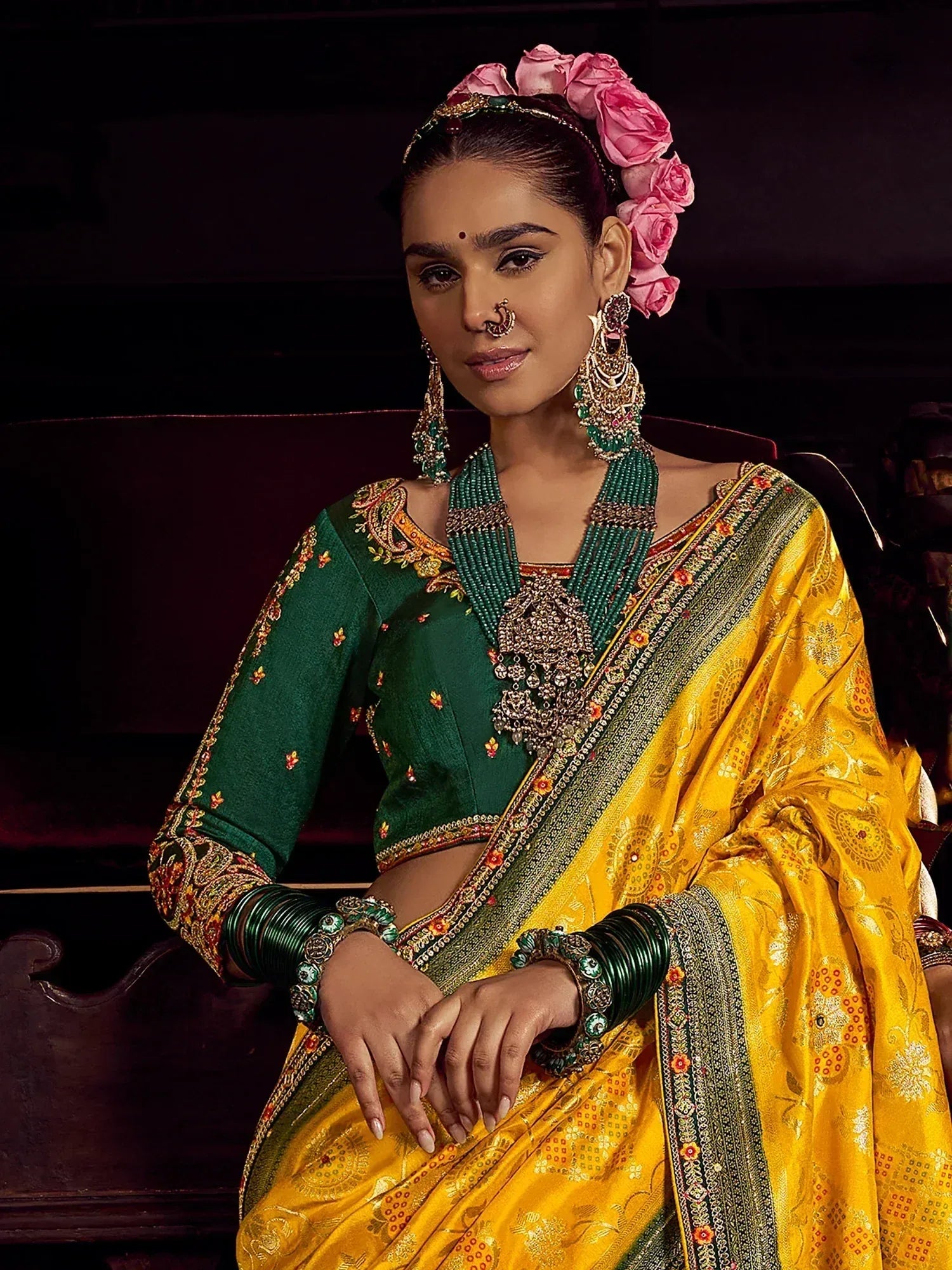 Elegant Indian ethnic wear: green blouse with gold embroidery, yellow saree, floral hair accessory, traditional jewelry