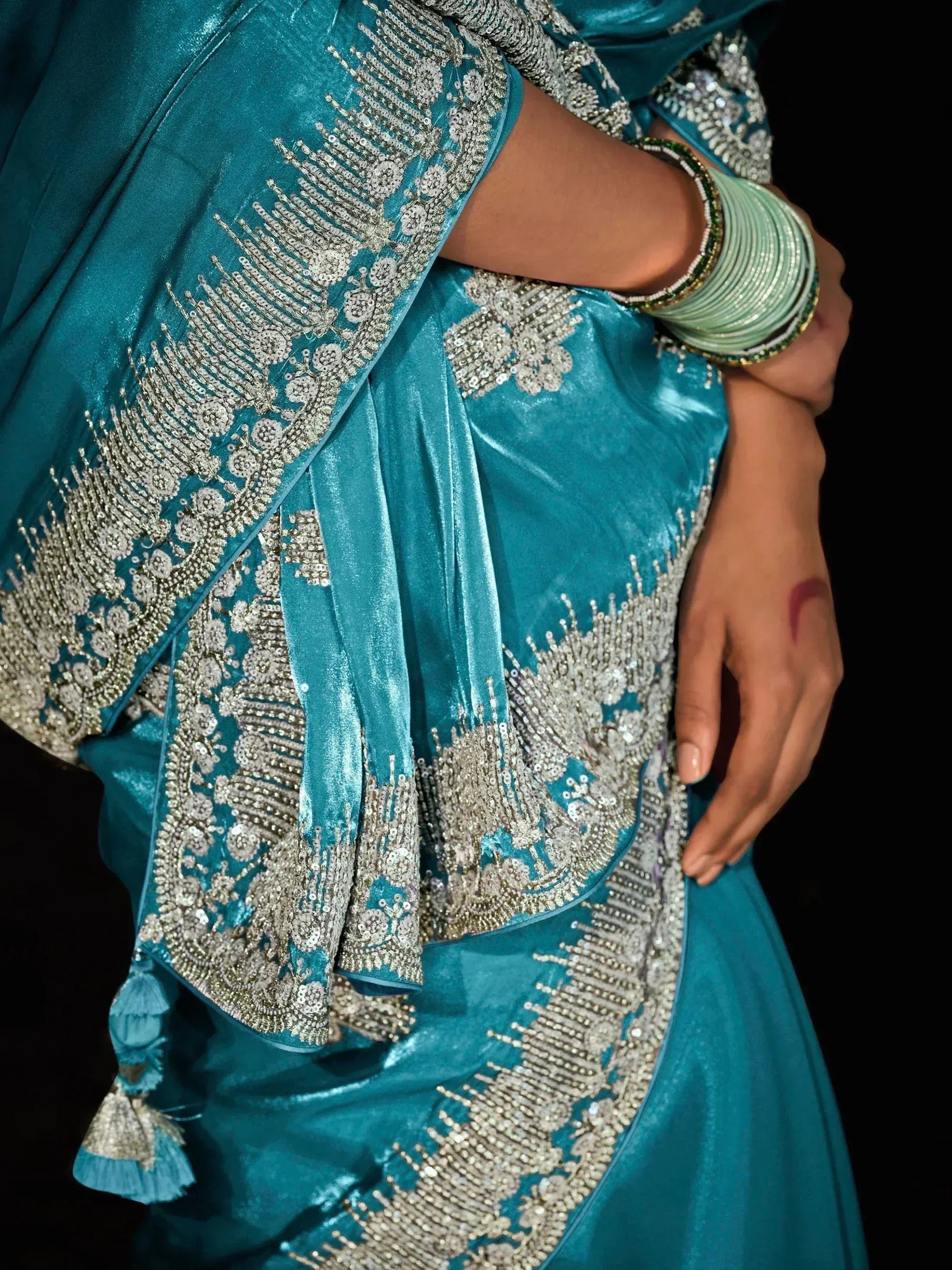 Teal velvet saree with silver embroidery and tassels, paired with green bangles for Indian ethnic wear.