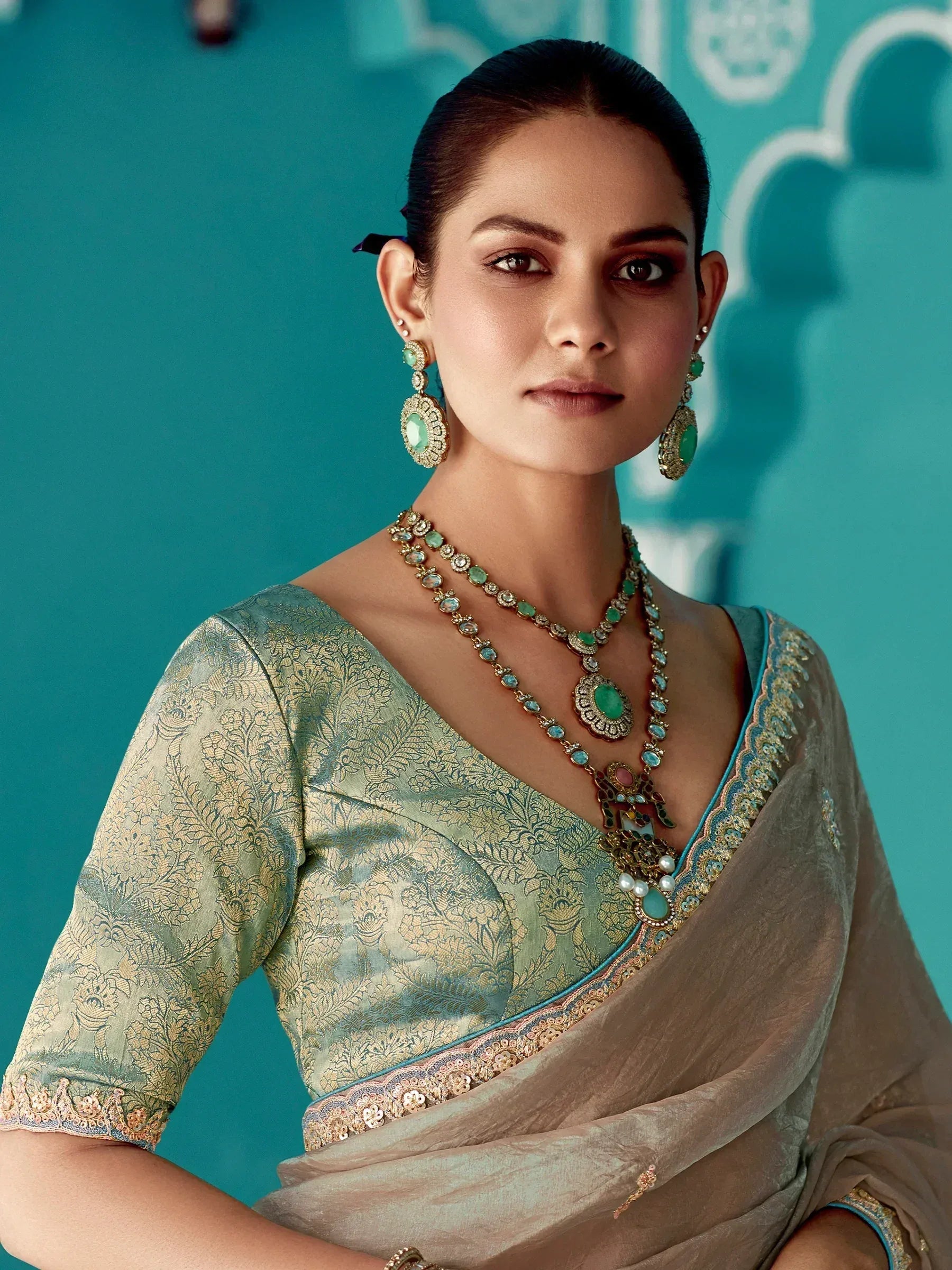 Elegant woman in designer saree with gold embroidery and green gemstone jewelry, perfect for Indian ethnic wear occasions.