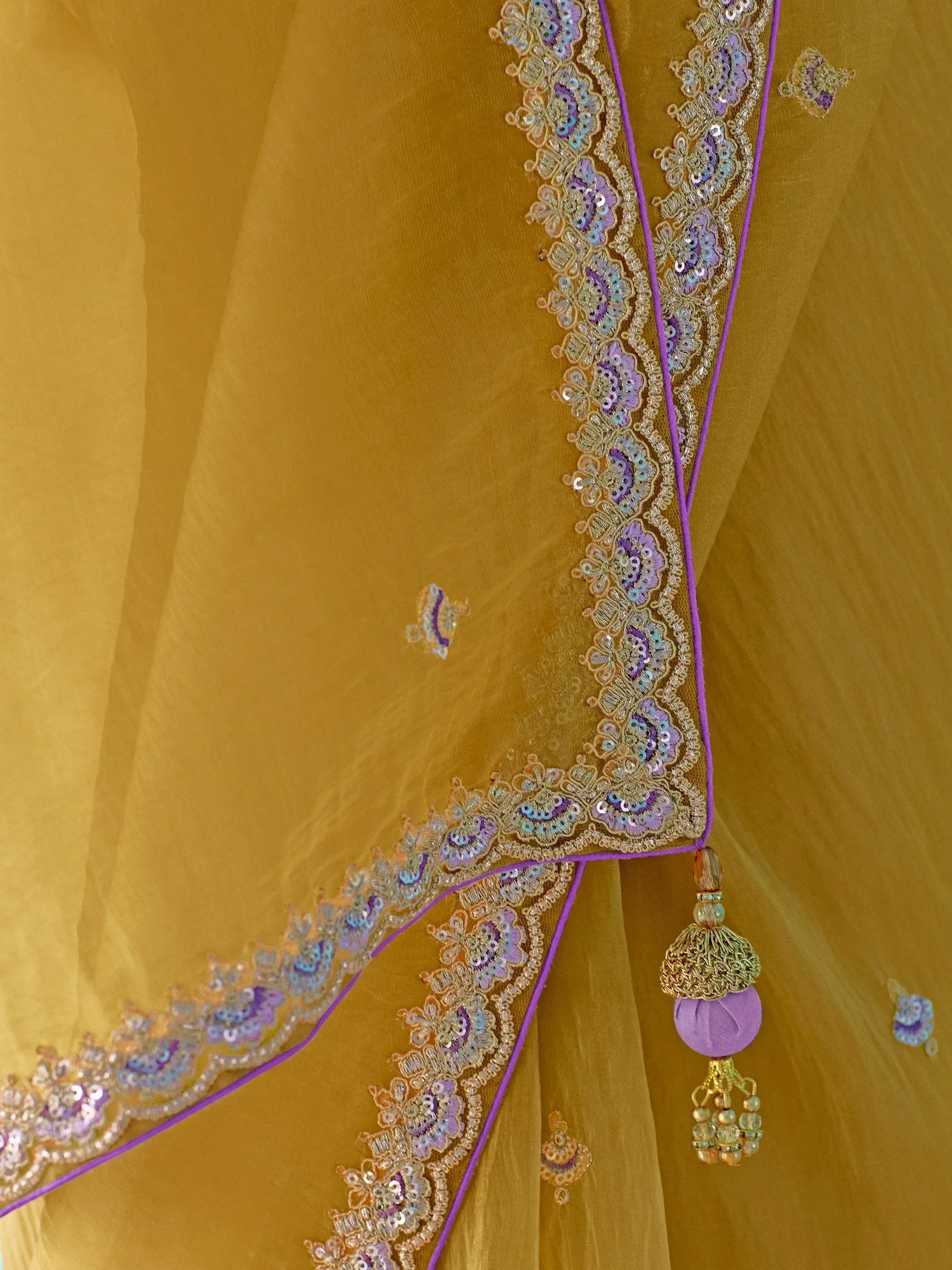 Golden ethnic saree with purple and gold sequin embroidery, tassels, and floral border details