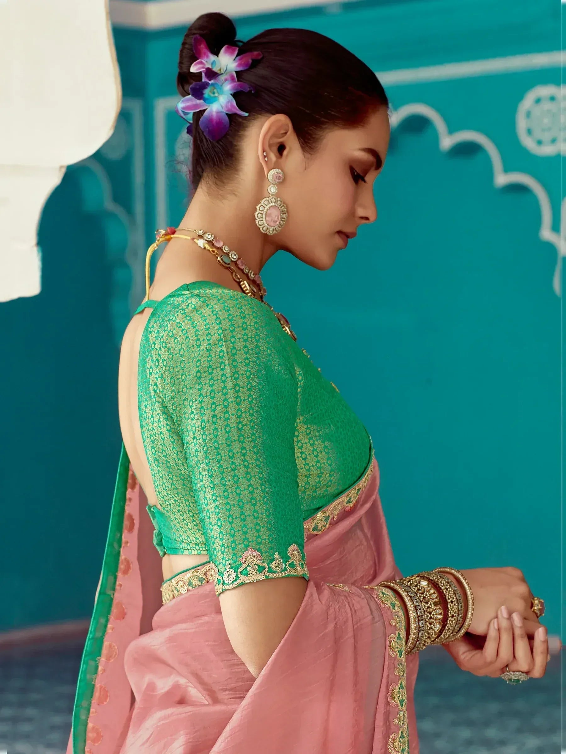 Woman in pink saree with green embroidered blouse, floral hair accessory, and traditional jewelry