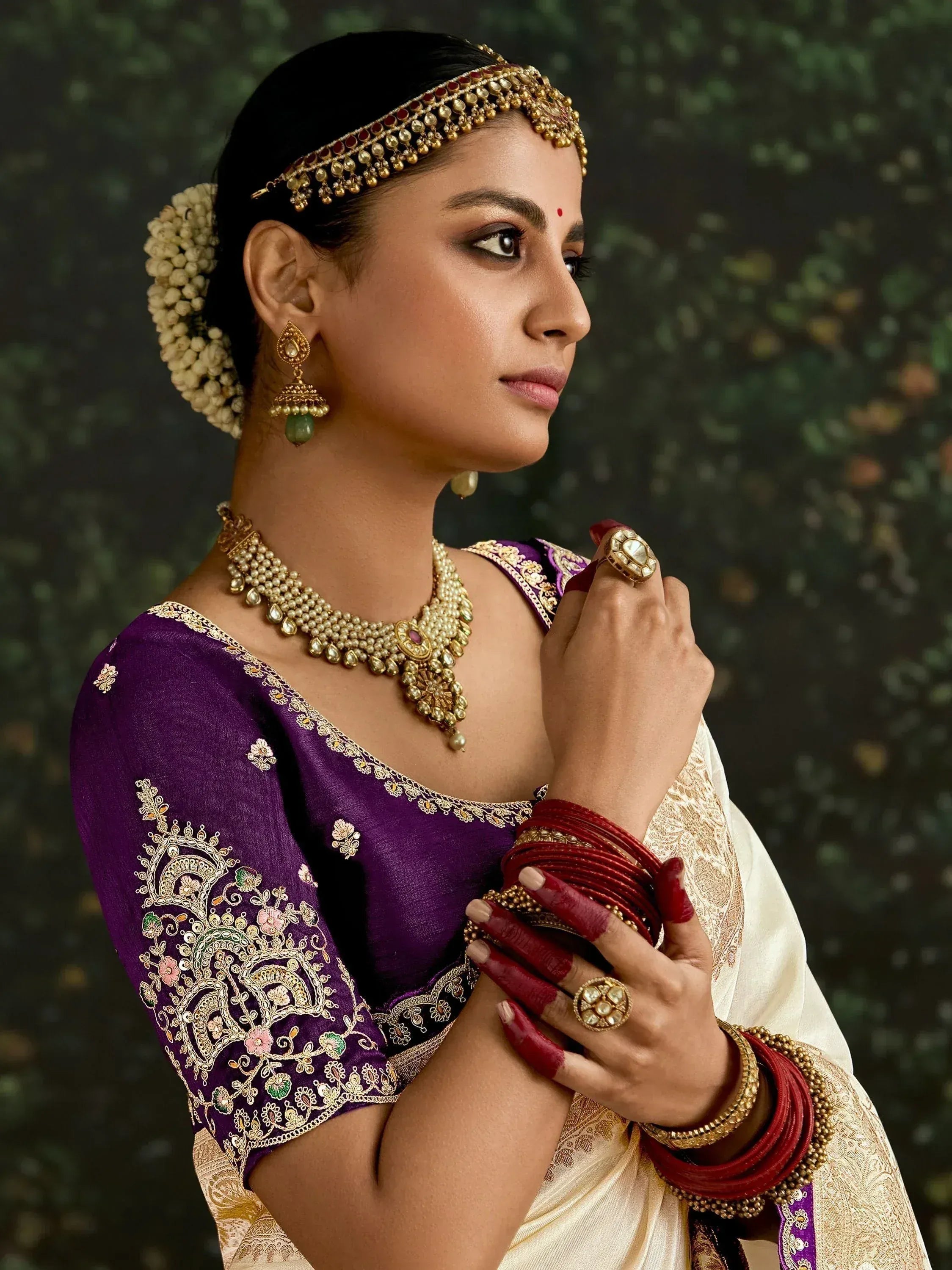 Woman in purple embroidered saree blouse with gold jewelry and floral hair accessory, traditional Indian ethnic wear