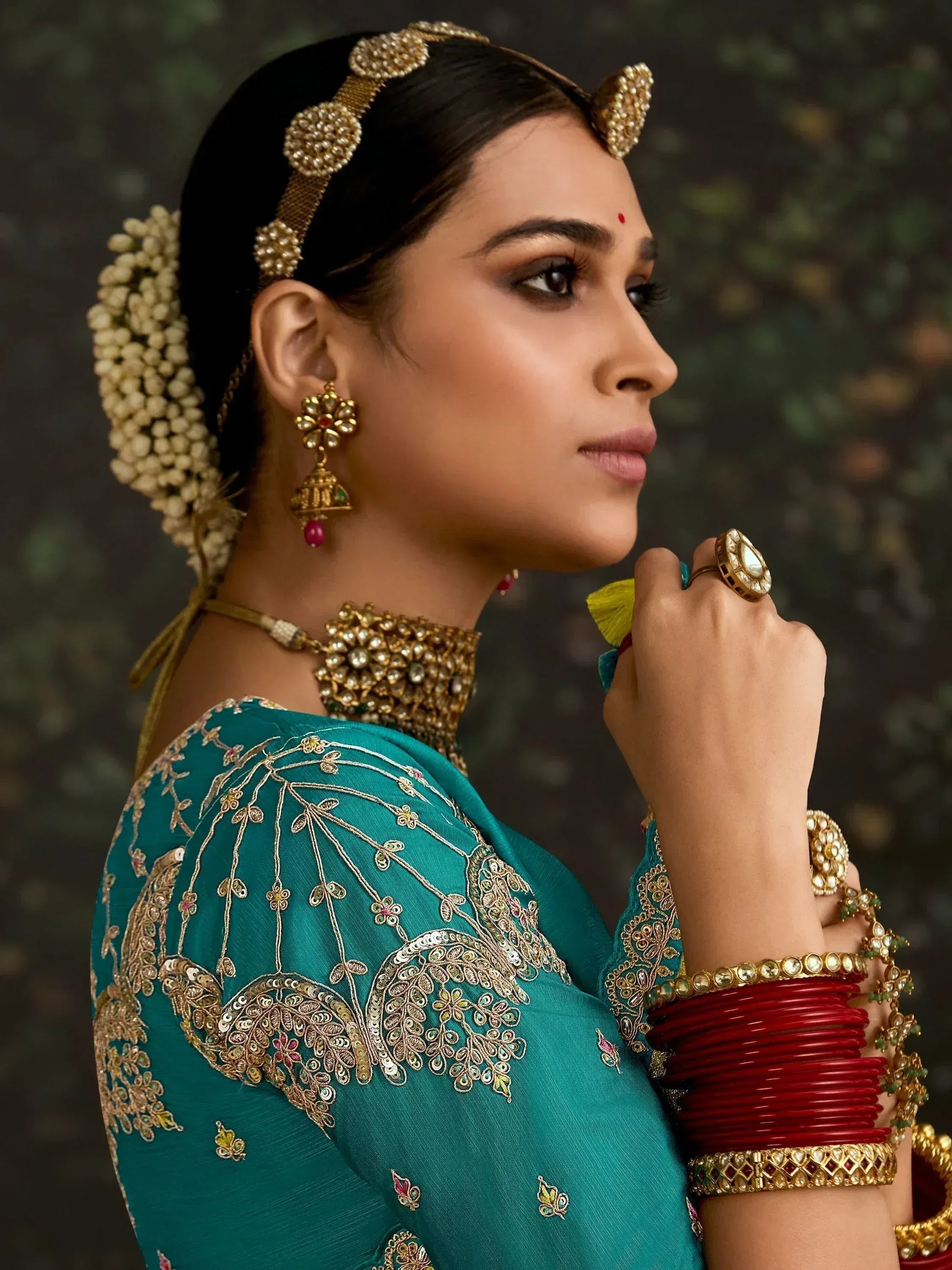 Woman in teal embroidered lehenga choli with gold jewelry and floral hair accessories