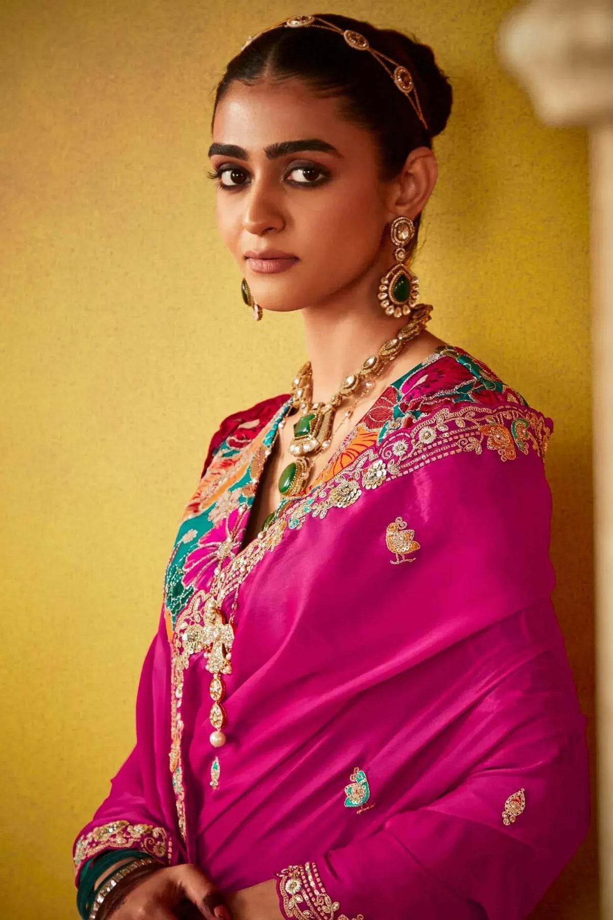 Woman in vibrant pink embroidered ethnic gown with gold jewelry, perfect for Indian weddings and festive occasions.