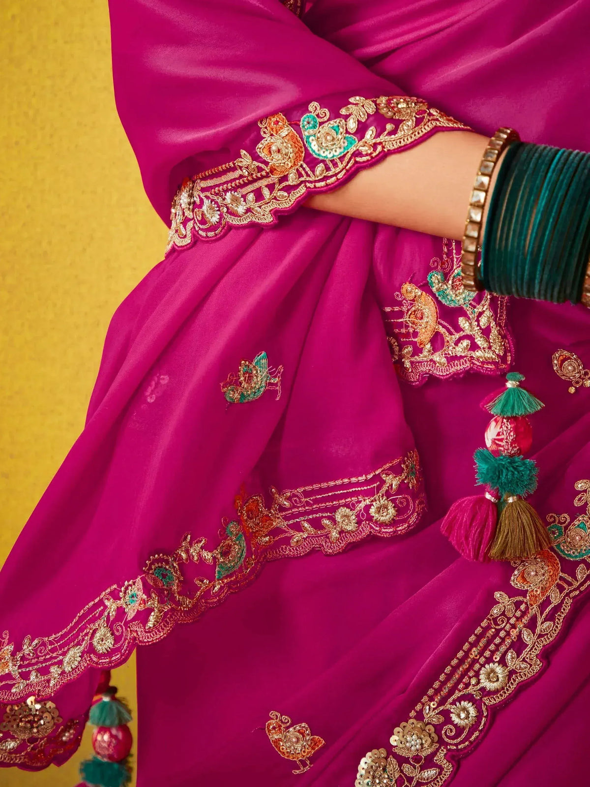 Fuchsia ethnic gown with gold embroidery, peacock motifs, and tassels, paired with green bangles.