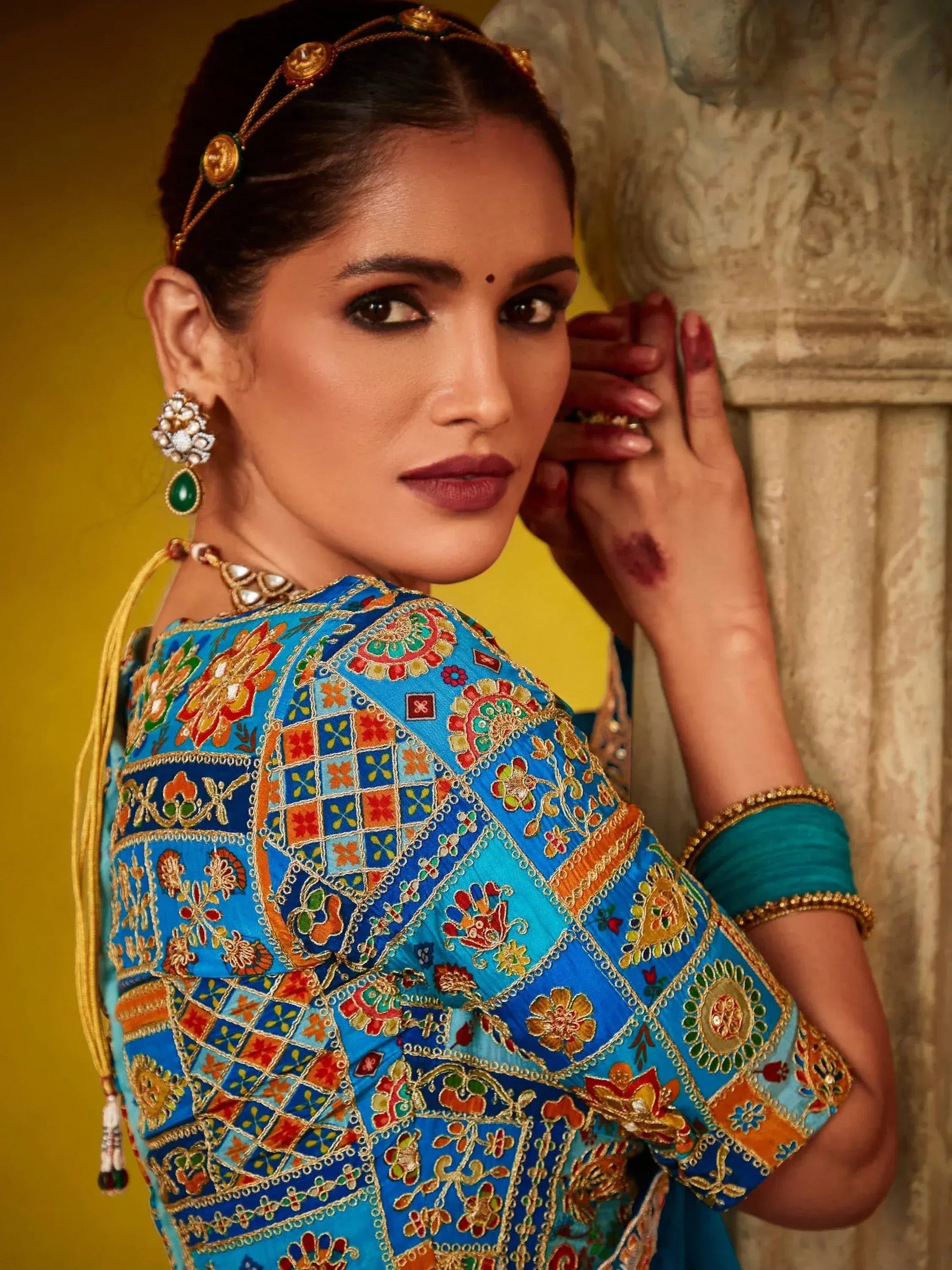 Woman in vibrant blue embroidered Indian ethnic wear with gold jewelry and traditional headpiece
