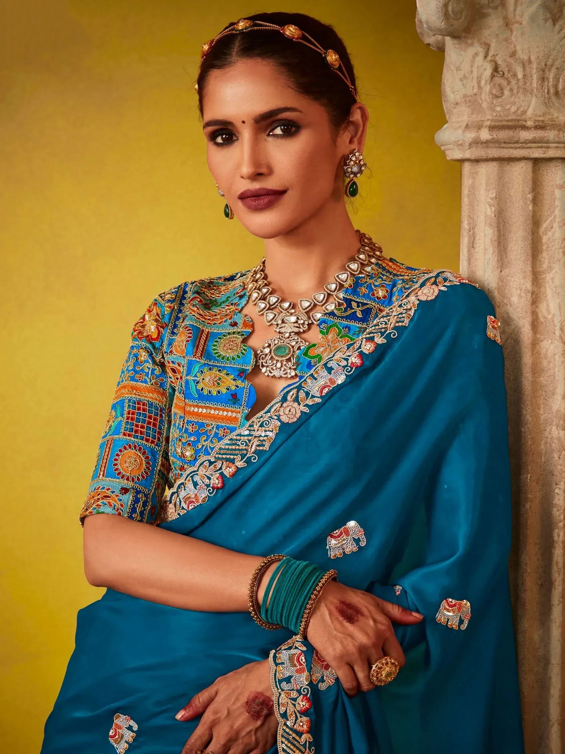 Woman in blue embroidered saree with elephant motifs, traditional Indian jewelry, and henna hands