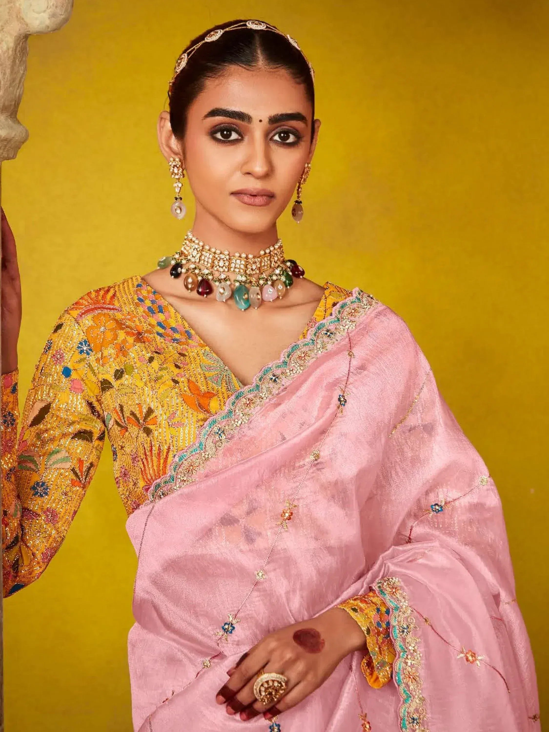 Woman in pink and yellow embroidered saree with traditional Indian jewelry, perfect for ethnic occasions.