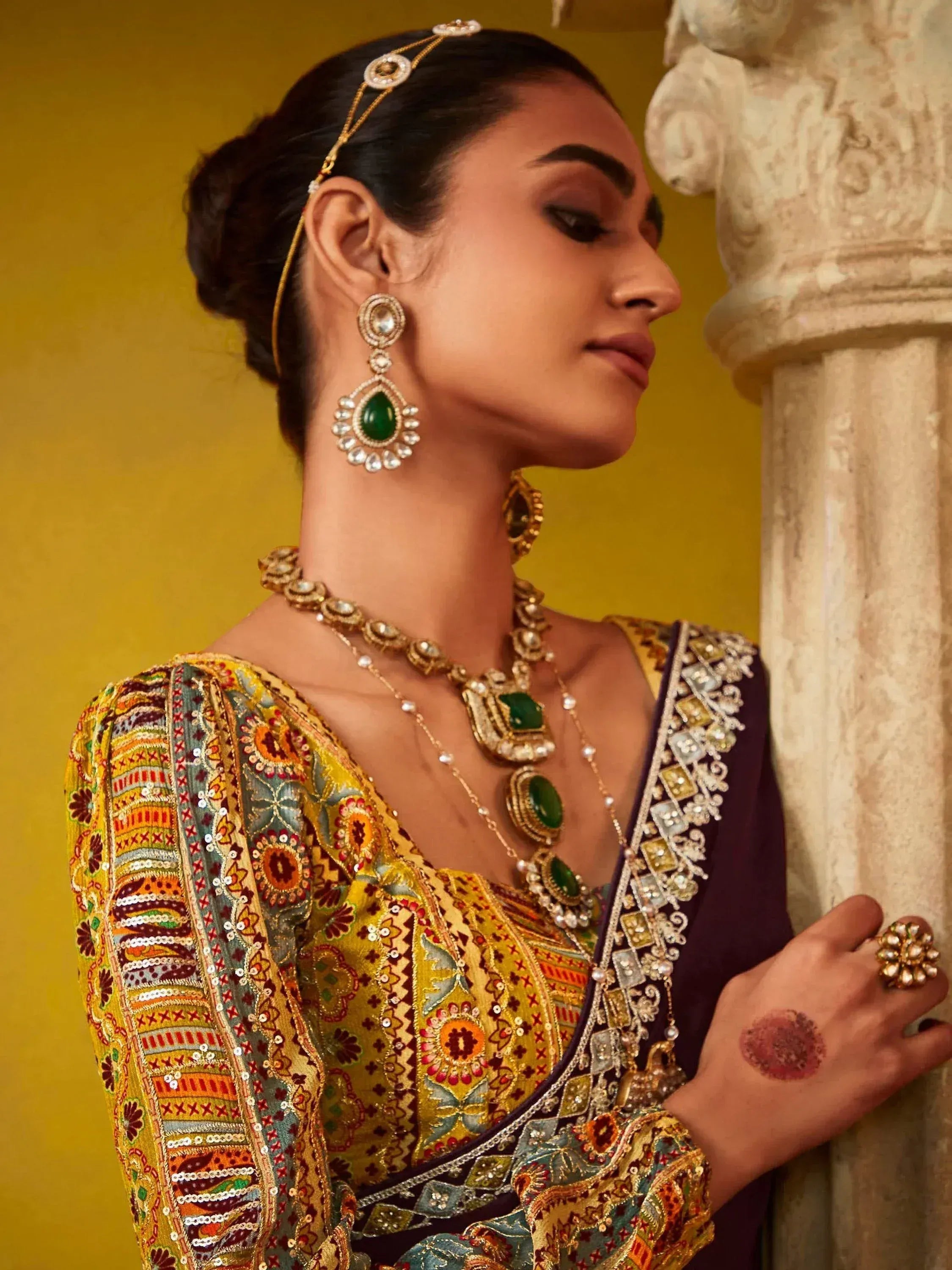 Woman in embroidered Indian ethnic wear with green gemstone jewelry and henna, styled for festive occasions
