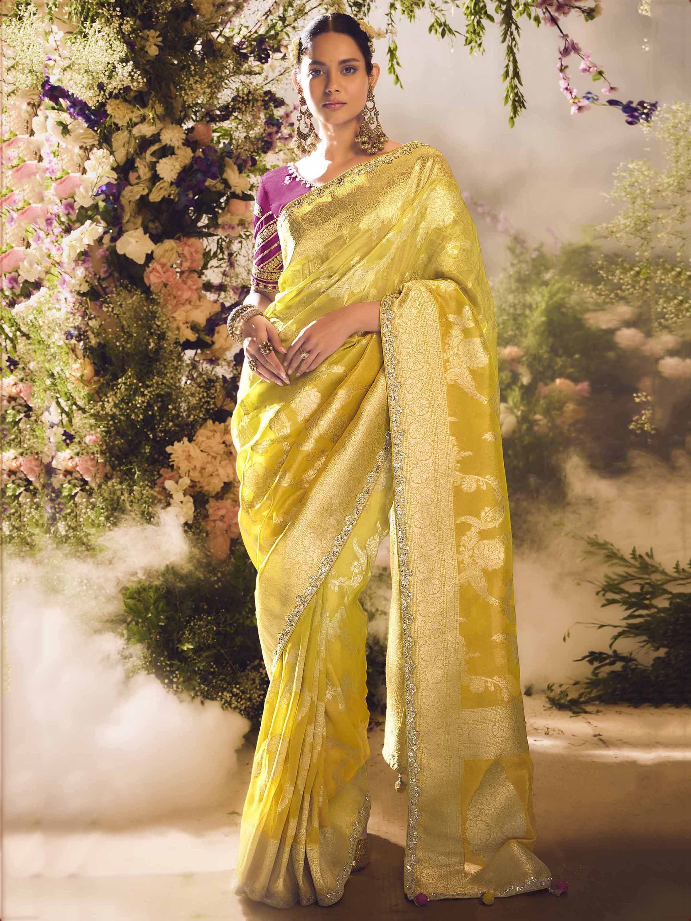 Yellow designer saree with gold embroidery, purple blouse, floral backdrop, ethnic wear