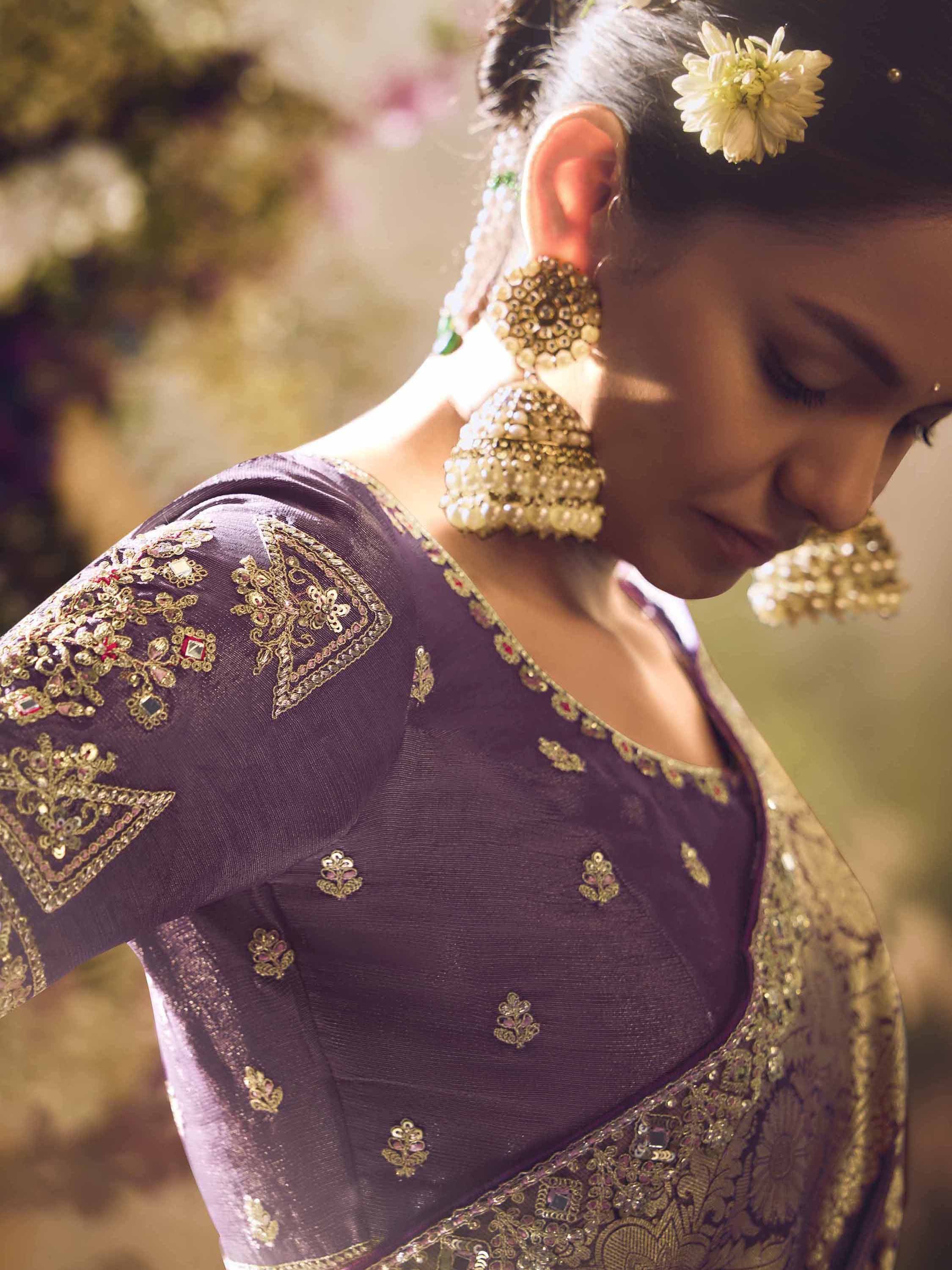 Purple embroidered saree blouse with gold detailing, jhumka earrings, and floral hair accessory