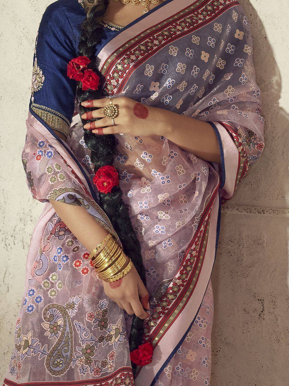 Woman in floral printed saree with blue blouse, gold jewelry, and red flower-adorned braid
