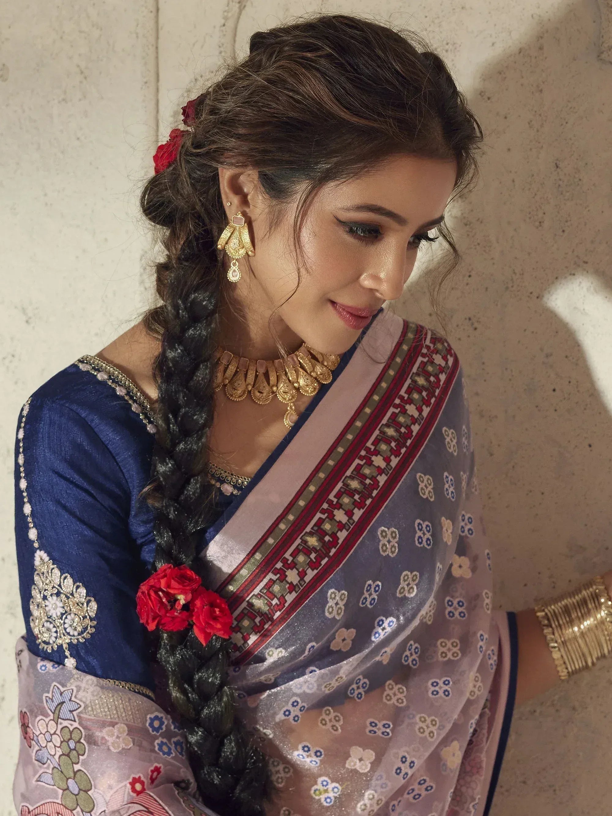 Woman in blue embroidered blouse and floral saree with gold jewelry, red flowers in braid