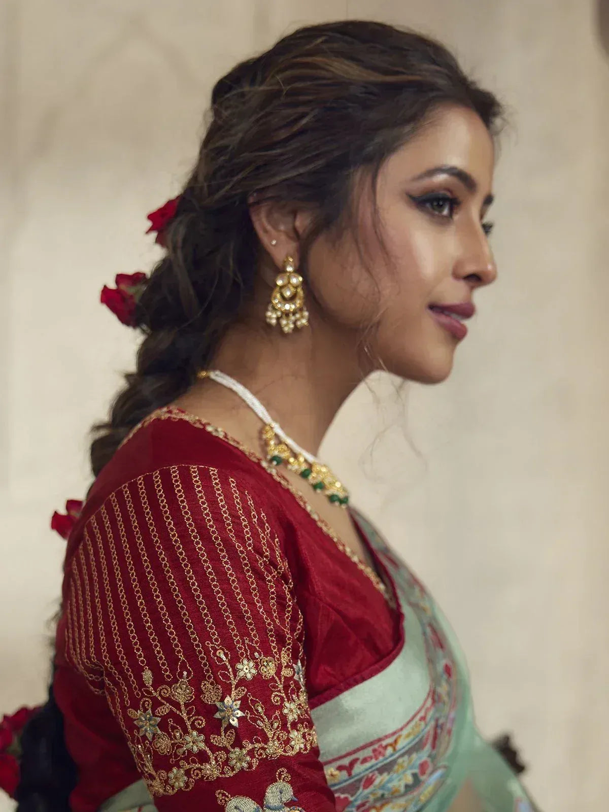 Woman in red embroidered blouse with gold jewelry and floral hair accessory, styled for Indian ethnic wear