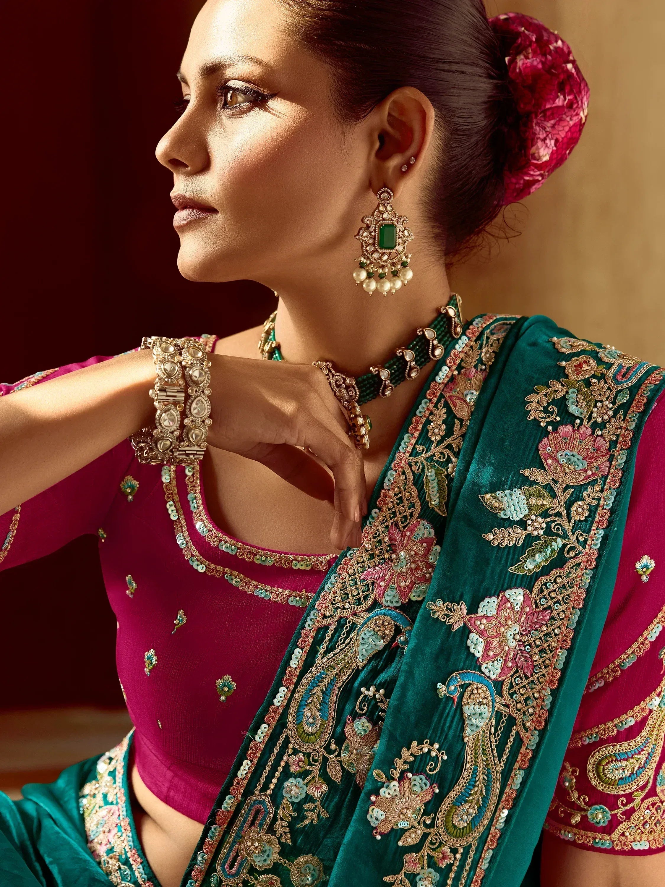 Elegant woman in embroidered teal saree with pink blouse, adorned with traditional jewelry.