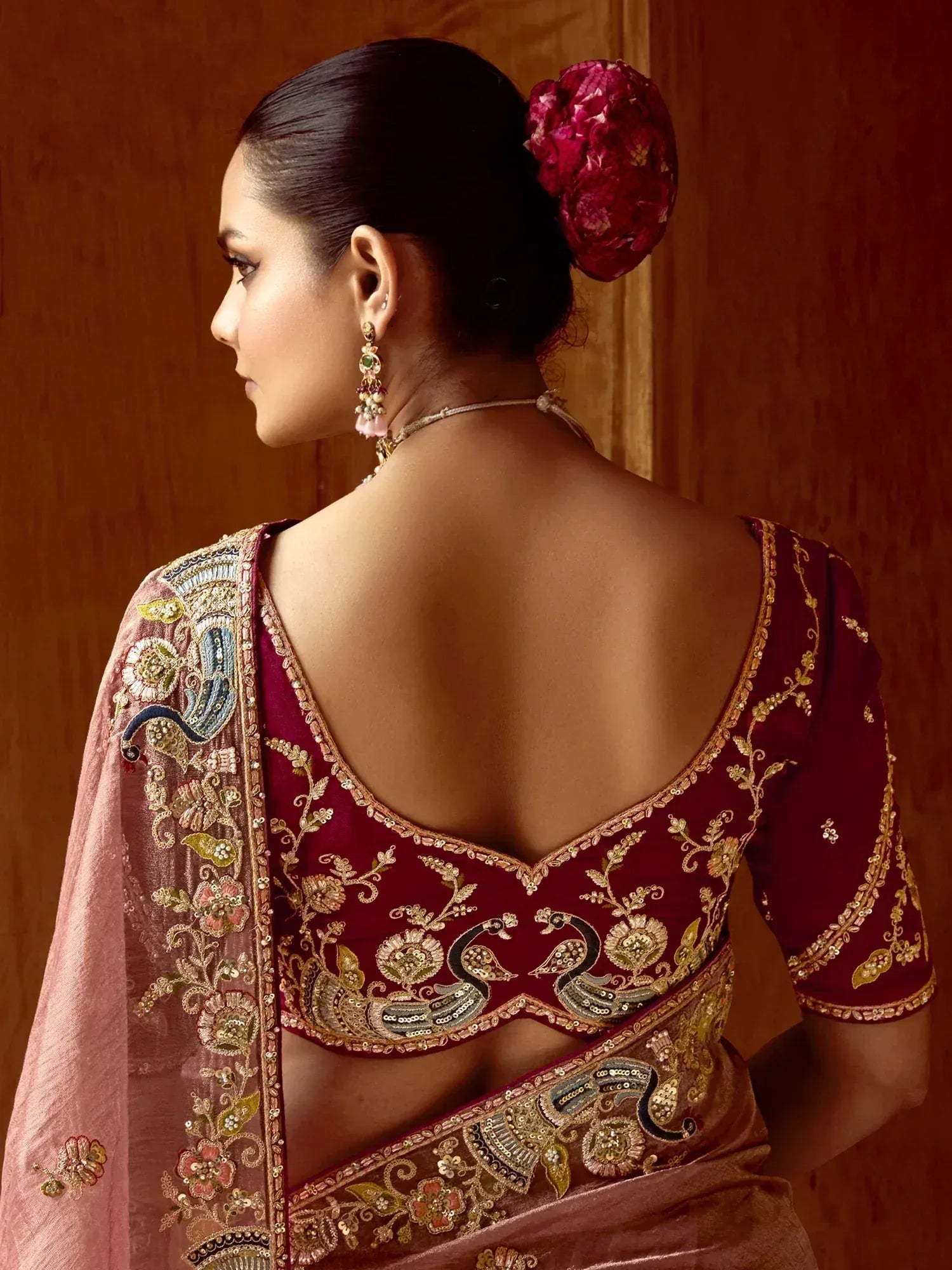 Elegant maroon saree with intricate gold embroidery and peacock motifs, paired with floral hair accessory.