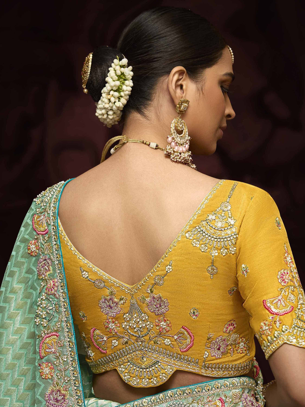 Yellow embroidered blouse with backless design, floral jewelry, and green saree for Indian ethnic wear