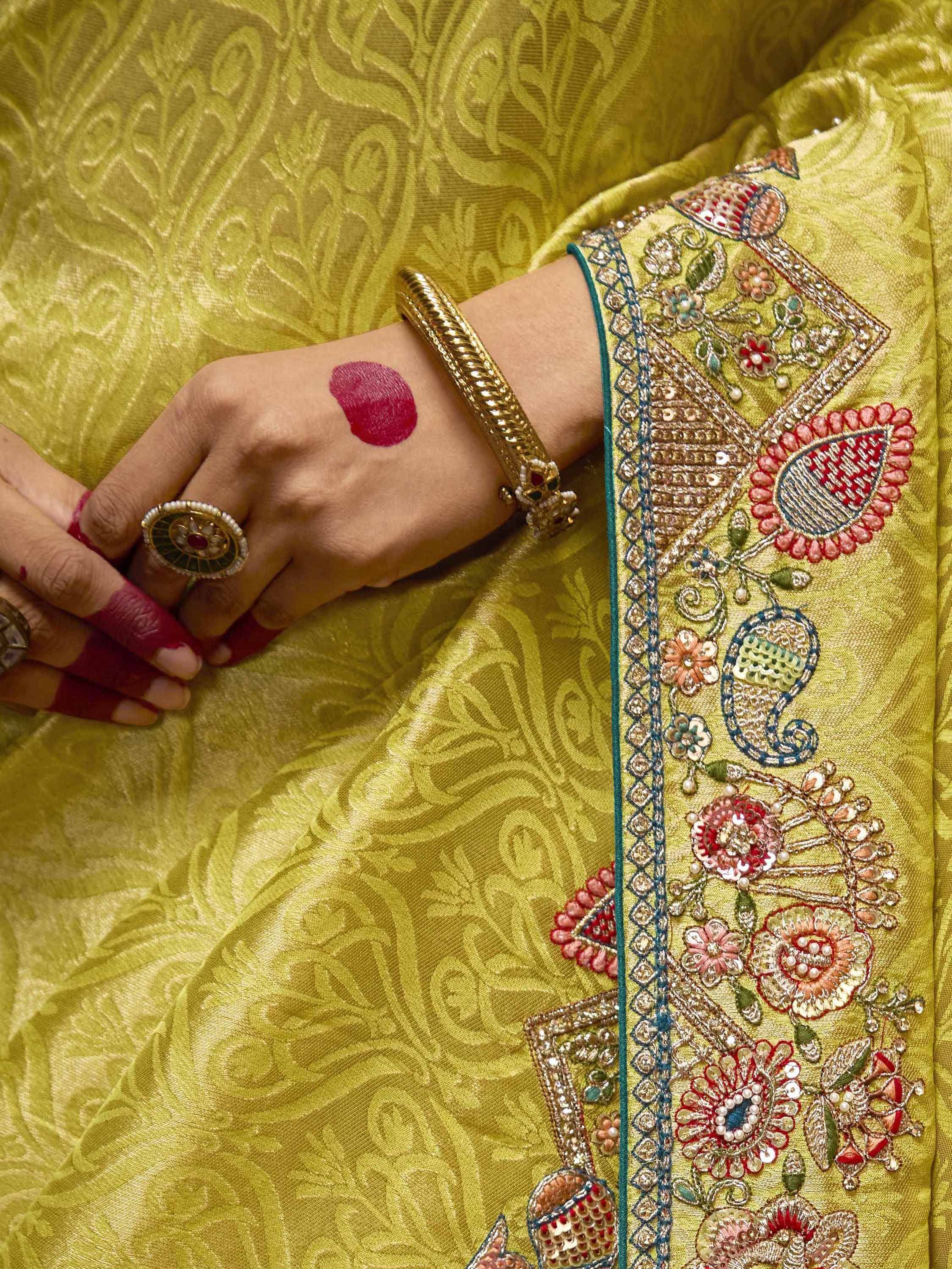 Yellow ethnic wear with floral embroidery, gold bangle, and traditional ring on hennaed hand