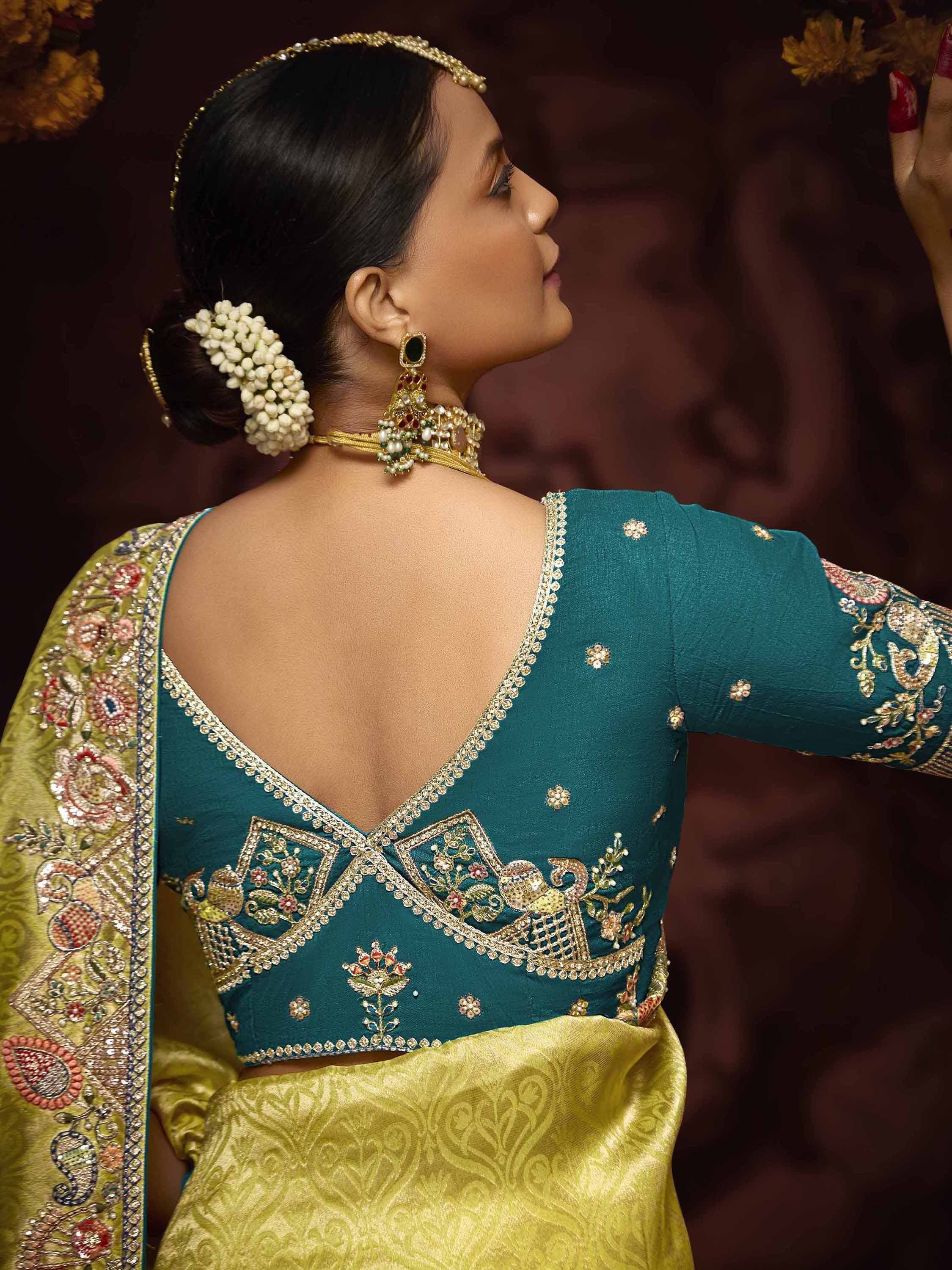 Teal embroidered blouse with gold detailing, paired with yellow saree and traditional jewelry for Indian ethnic wear.