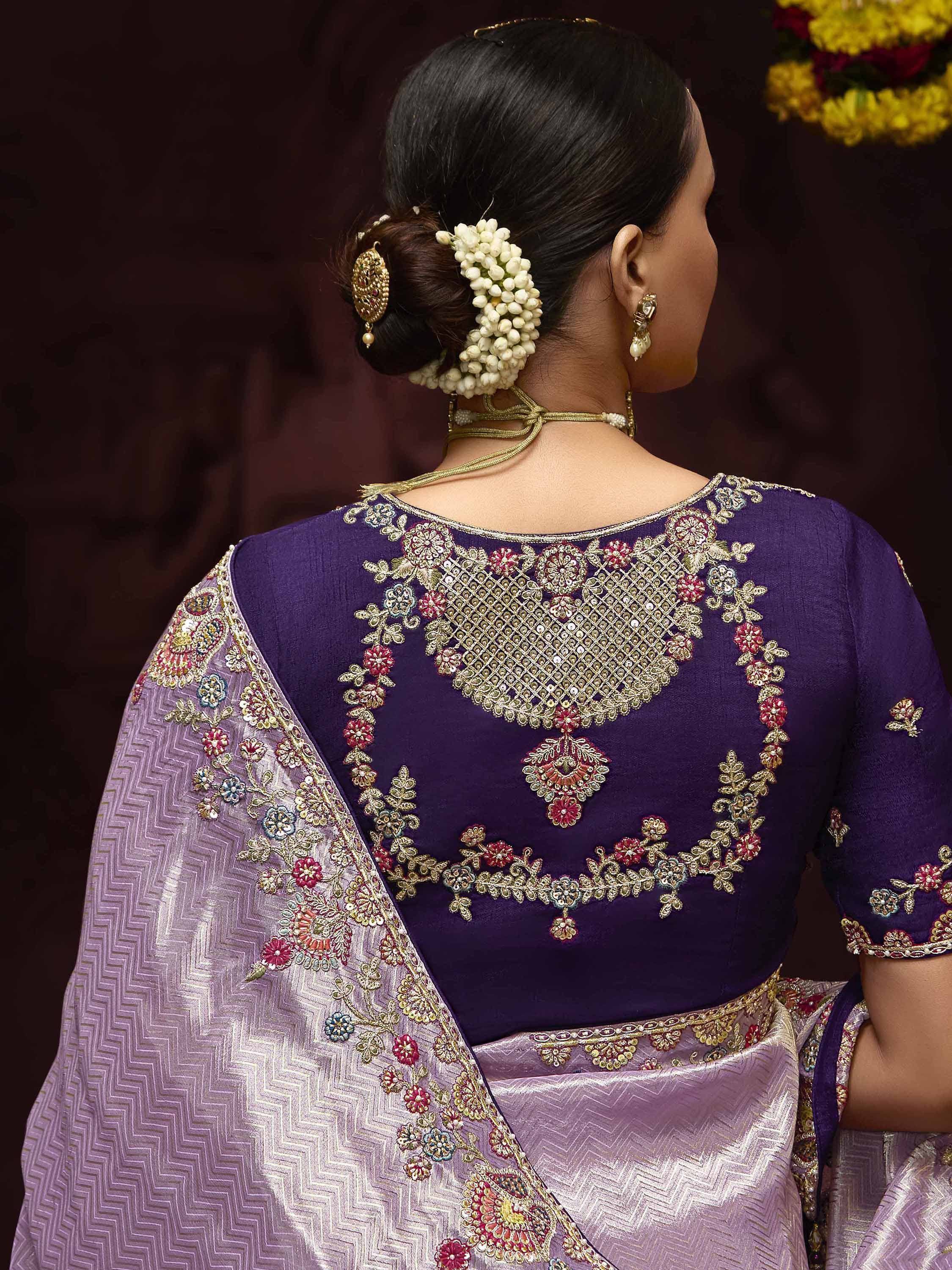 Purple designer saree blouse with intricate floral embroidery and back neck detailing, paired with traditional hair accessories.