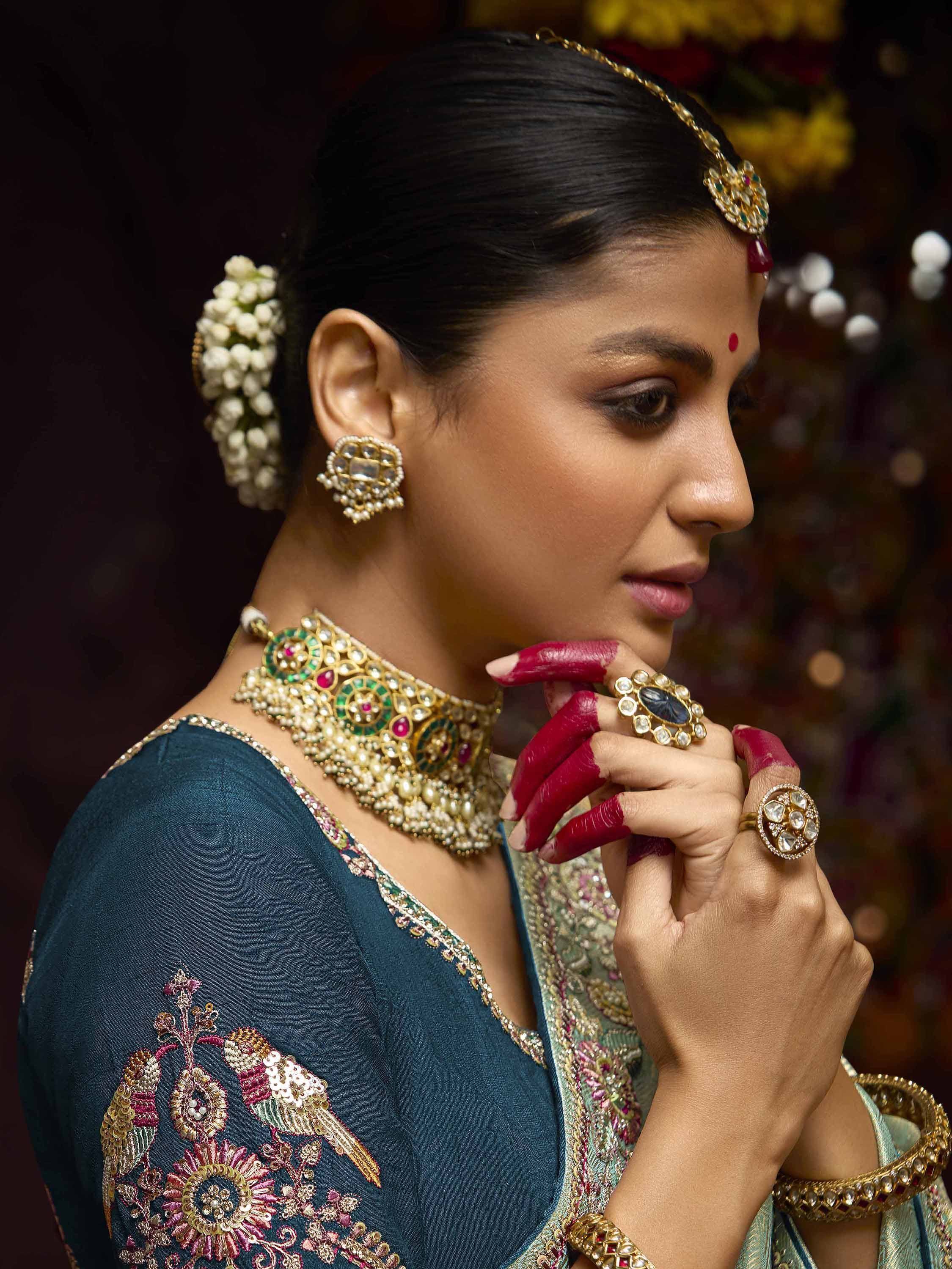 Indian bride in teal embroidered lehenga with gold jewelry and floral hair accessory