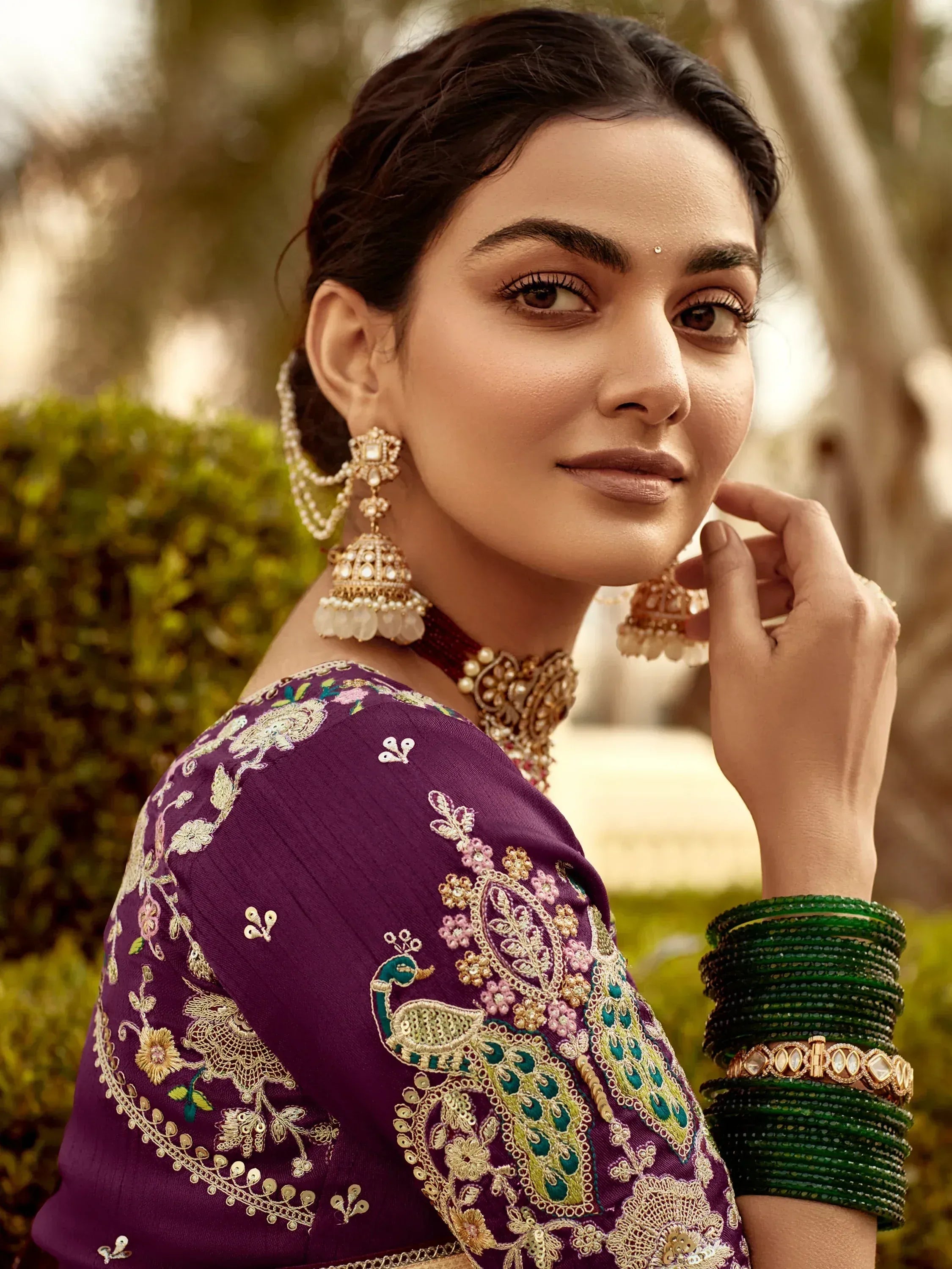 Purple embroidered lehenga choli with peacock design, paired with gold jewelry and green bangles