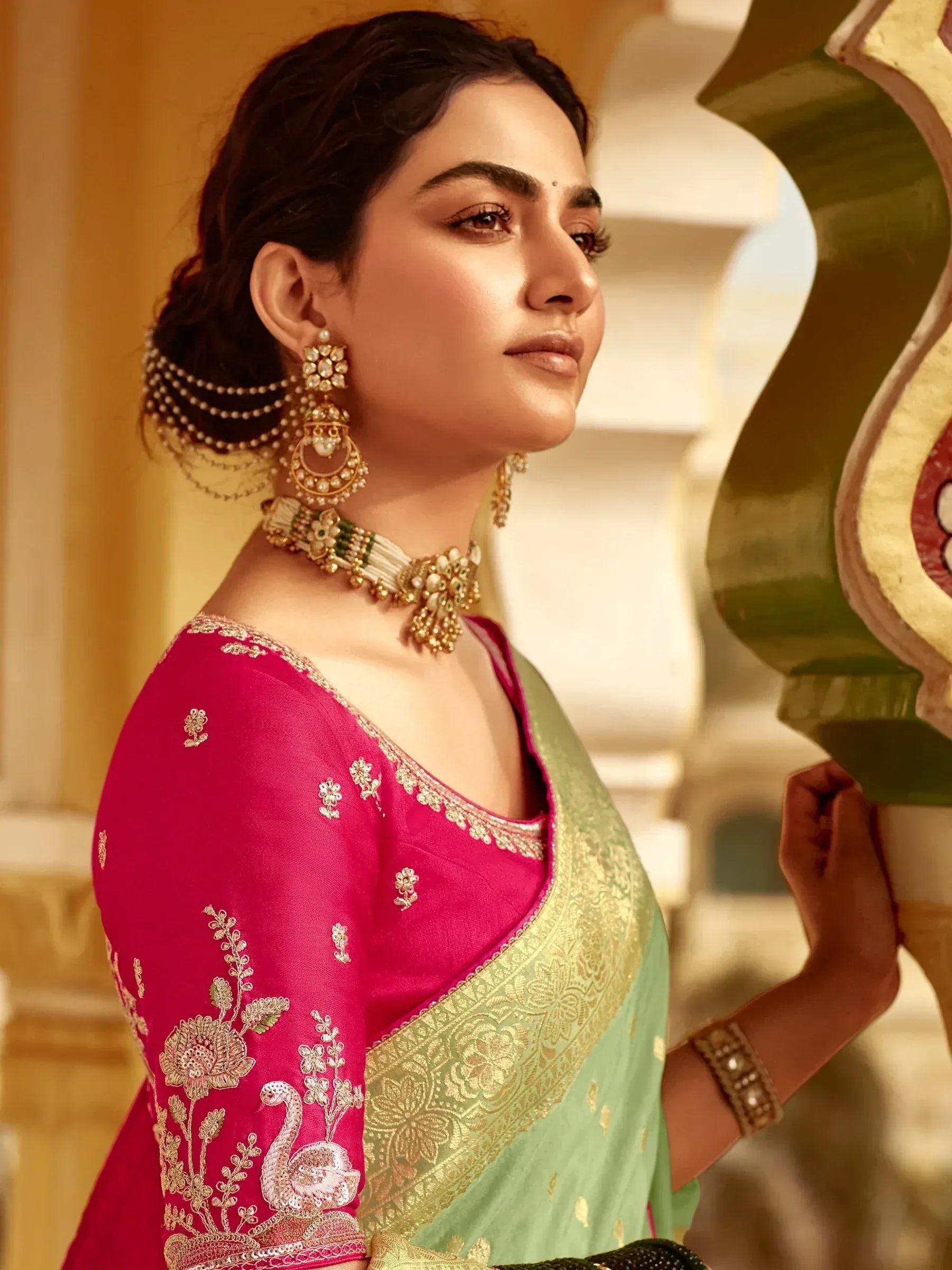 Elegant woman in pink and green embroidered saree with gold jewelry, showcasing Indian ethnic wear.