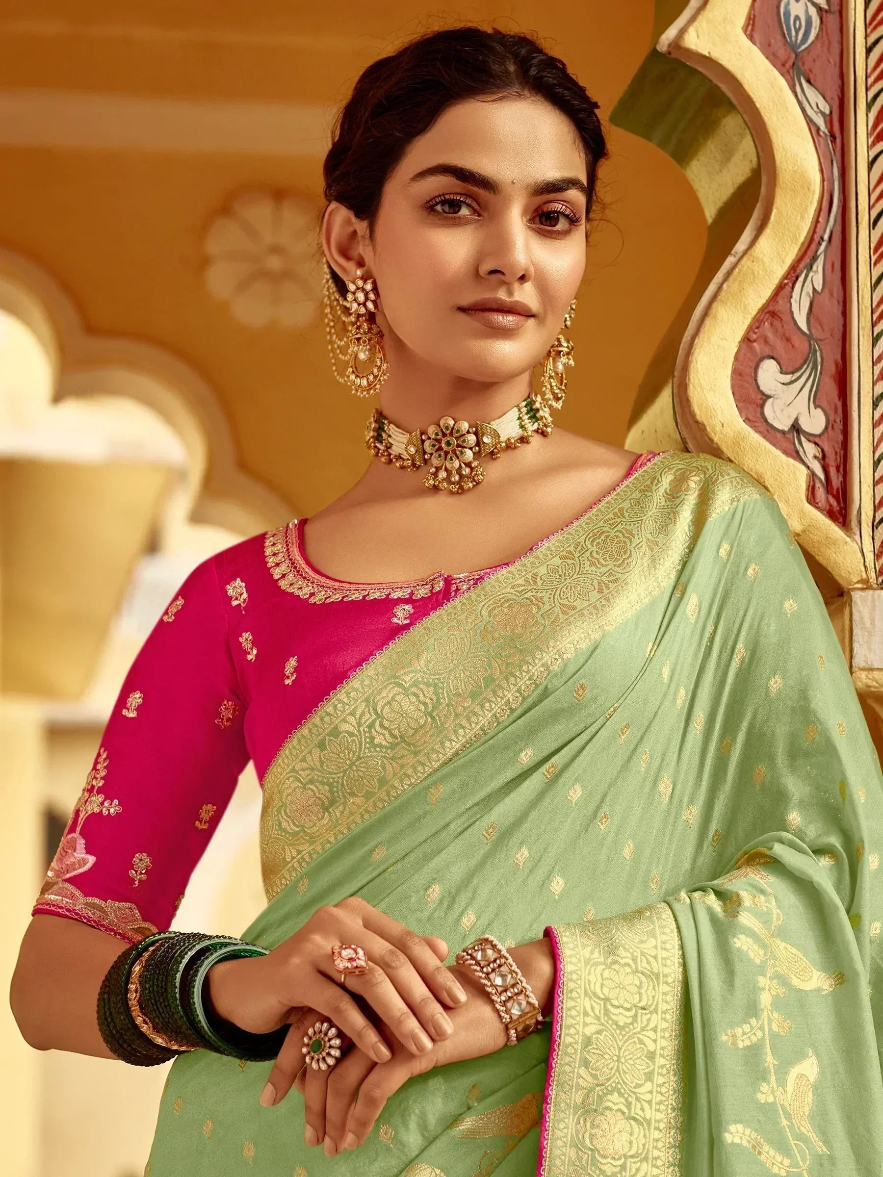 Woman in mint green saree with gold embroidery and pink blouse, styled with traditional Indian jewelry for festive occasions.