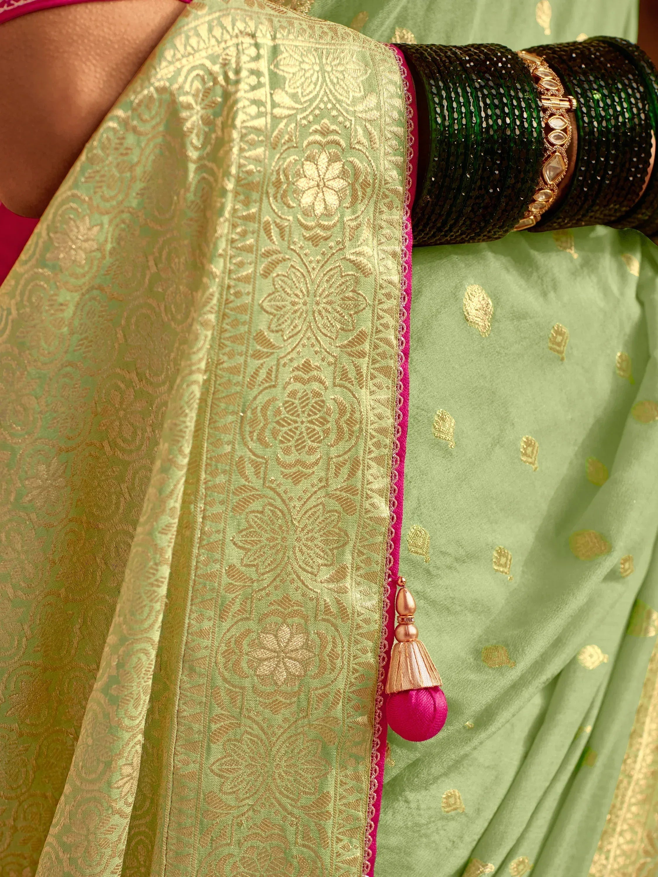 Elegant green saree with gold floral embroidery and pink tassel, paired with green bangles.