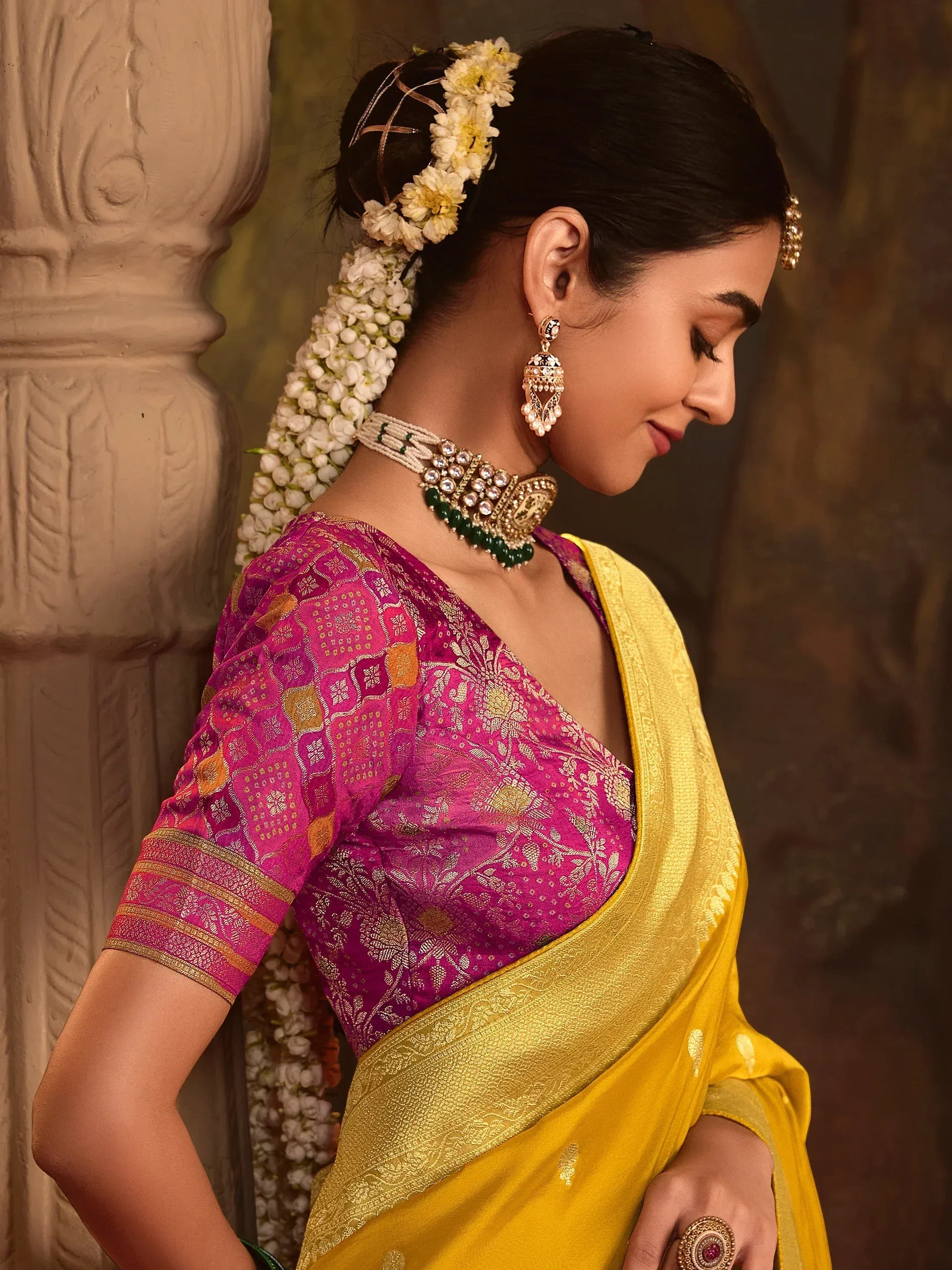 Woman in vibrant yellow saree with pink blouse, floral hair adornment, and traditional Indian jewelry