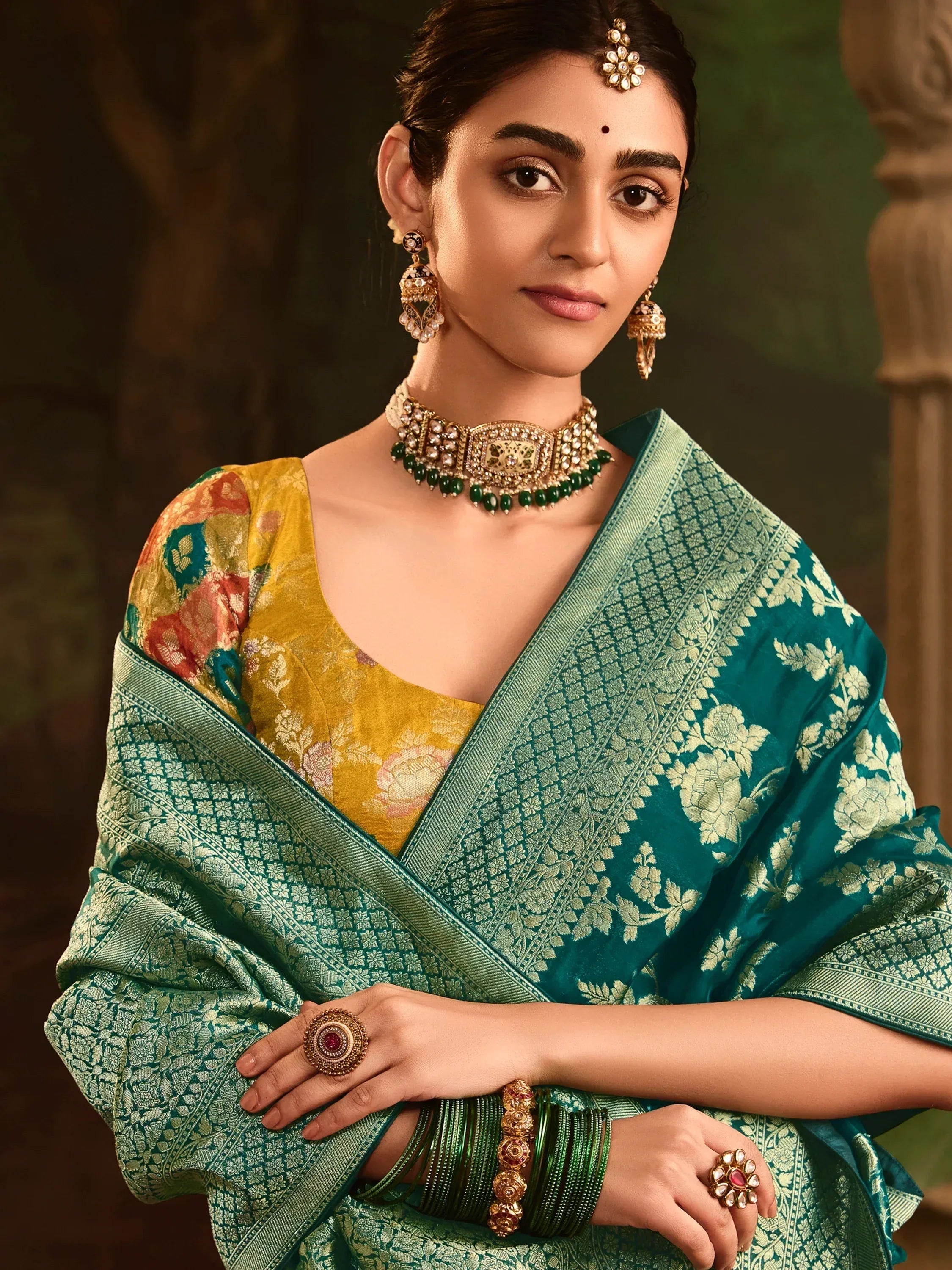 Elegant woman in teal floral saree with gold jewelry, showcasing traditional Indian ethnic wear.