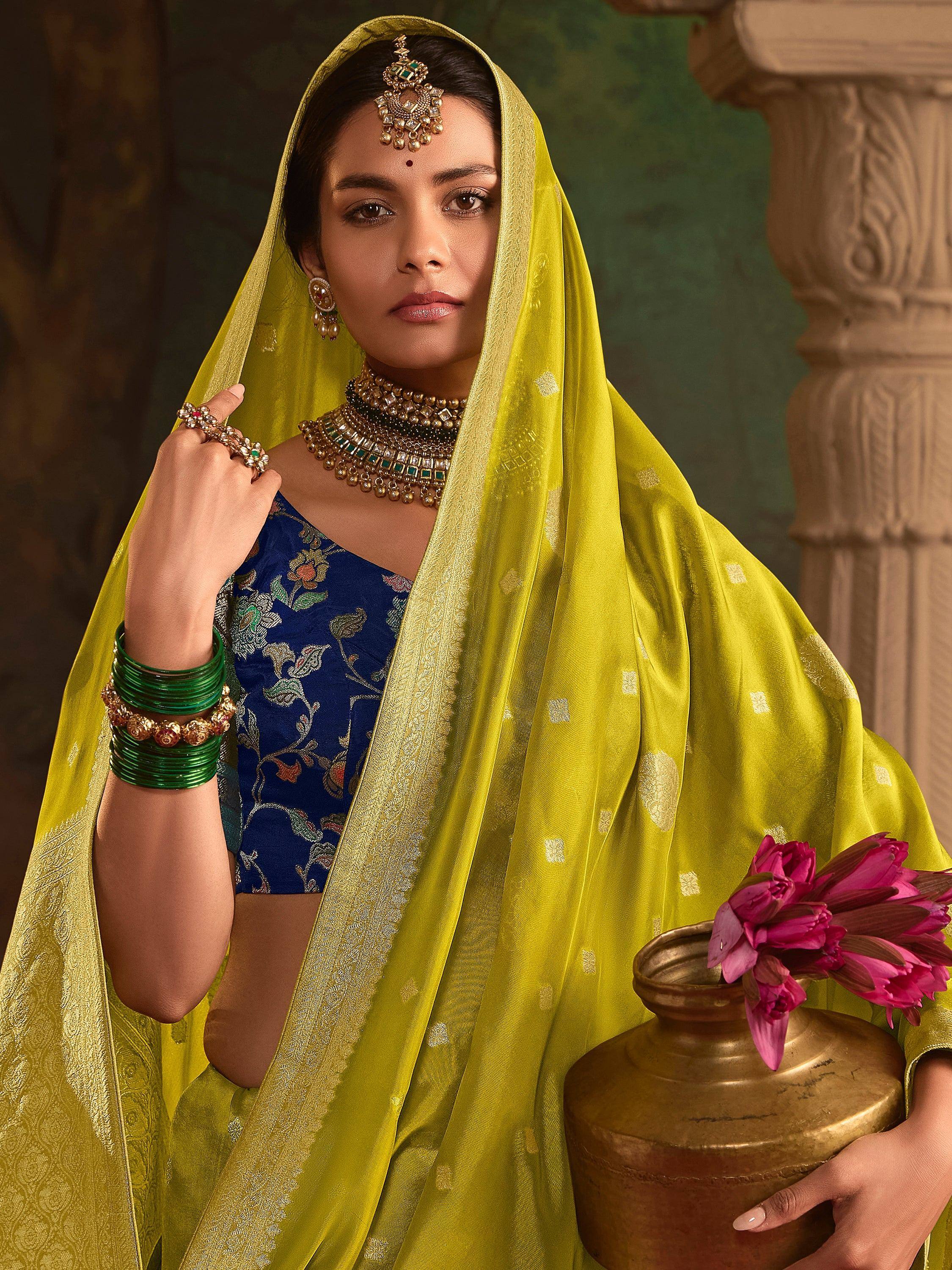Elegant woman in blue floral blouse with yellow dupatta, traditional Indian ethnic wear, holding brass pot with pink flowers
